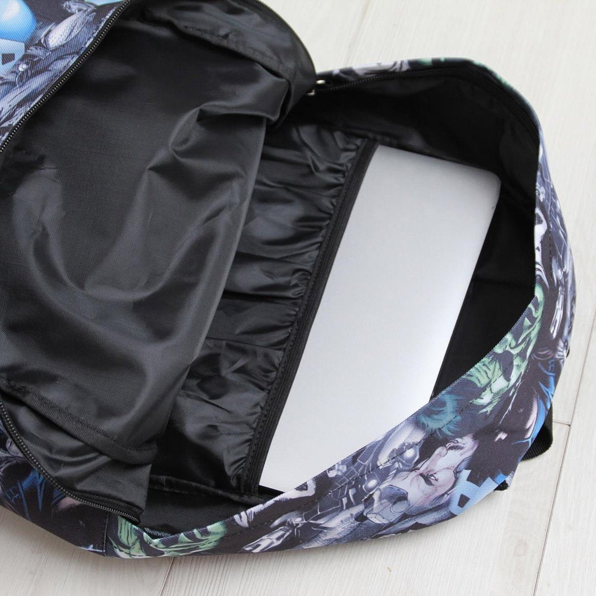 Mochila de Batman abierta con un portátil dentro. Diseño de cómic. El fondo es un suelo de madera clara.