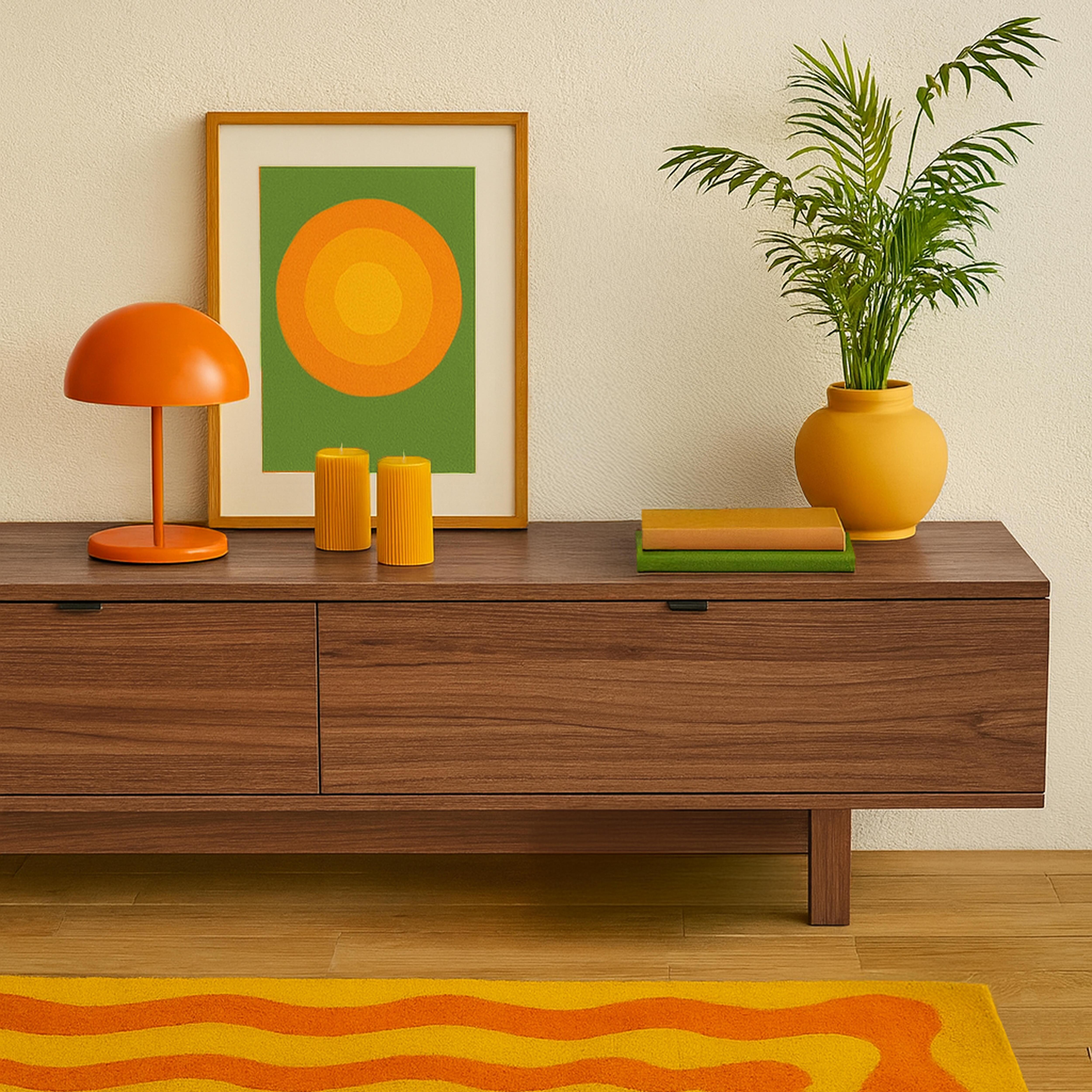Ein Raum mit Holzschrank, Kunst, Lampe, Pflanze und gemustertem Teppich. Farben sind Orange, Gelb, Grün und Braun.