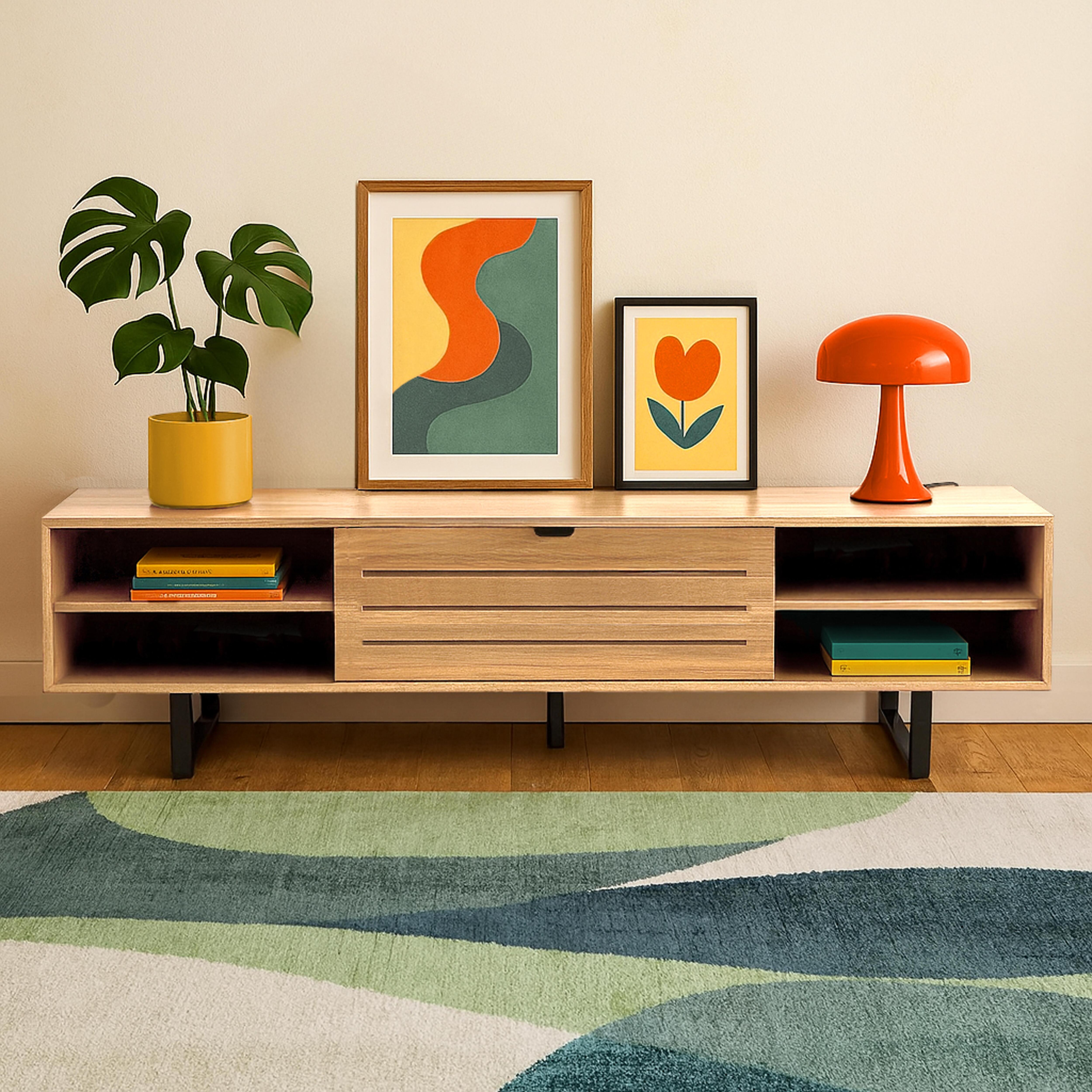 Ein Holzschrank mit Kunst, Lampe und Pflanze steht auf einem gemusterten Teppich. Zwei Bilder hängen an der Wand. Ein gelber Topf hält eine Pflanze.