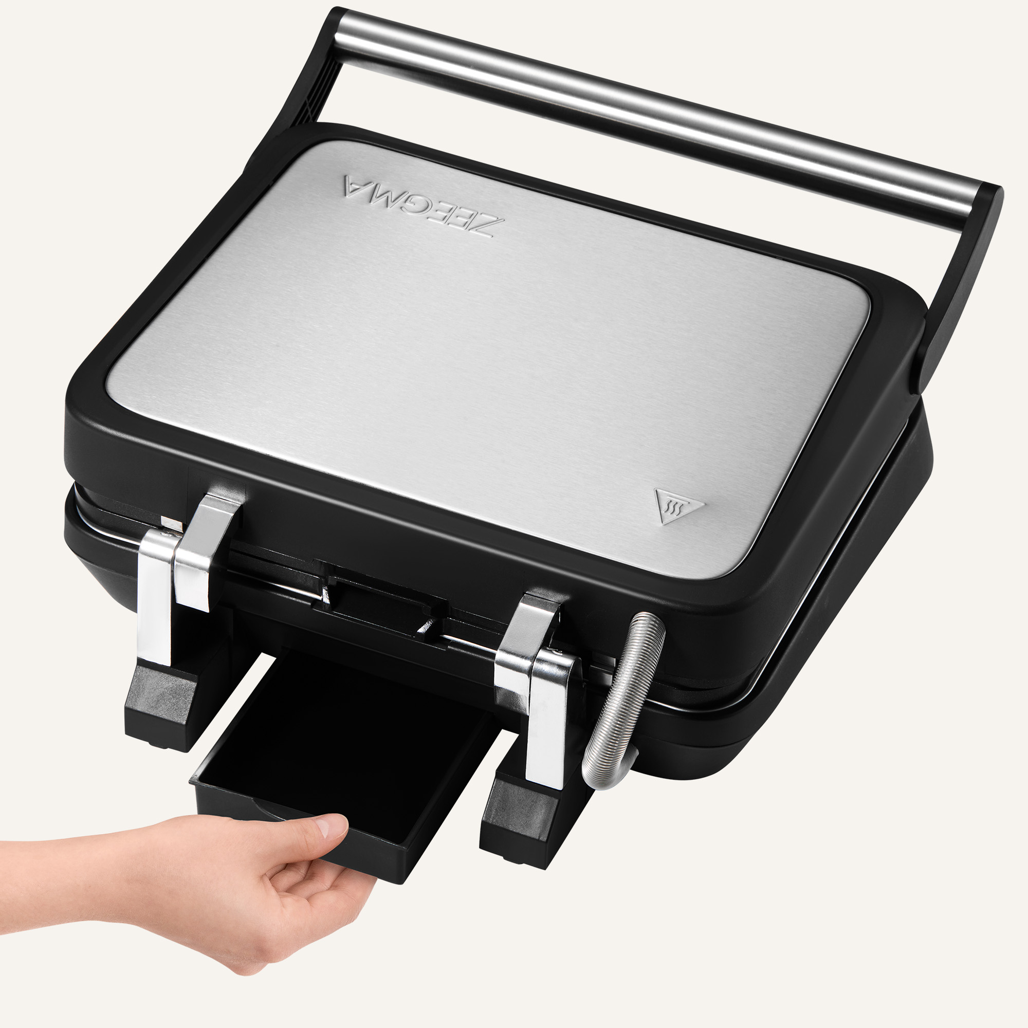 A person's hand pulls a black tray from a black and silver sandwich maker. The maker has a stainless steel top.