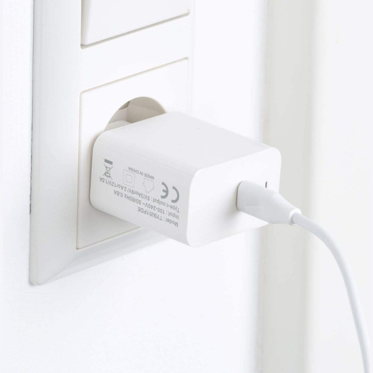 Een witte telefoonlader die in een stopcontact zit. De lader heeft een witte kabel die naar rechts loopt.