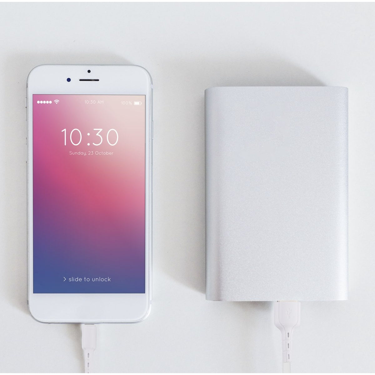 Een witte smartphone en een zilveren powerbank zijn verbonden door witte oplaadkabels op een wit oppervlak.