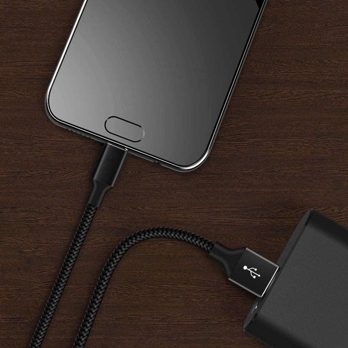 Smartphone opladen met een zwarte gevlochten kabel aangesloten op een voedingsadapter op een houten oppervlak.