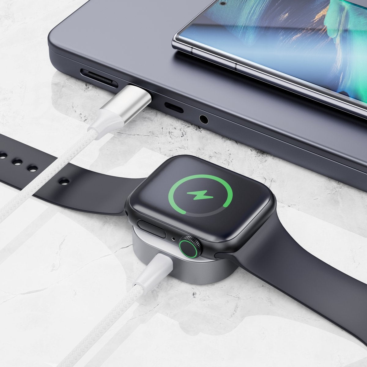 A black Apple Watch on a charging dock, with a phone on top. A cable connects the watch and phone to a power source.