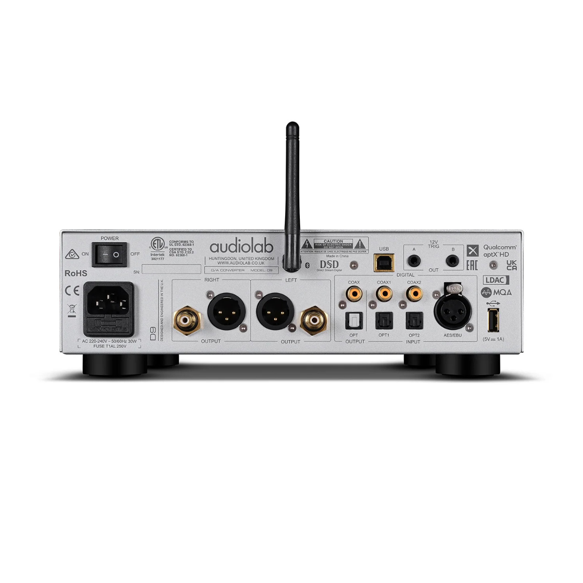 Zilveren achterpaneel van audioapparaat met diverse in-/uitgangen, labels en een aan/uit-schakelaar. Antenne bovenop. Zwarte voedingskabelingang.