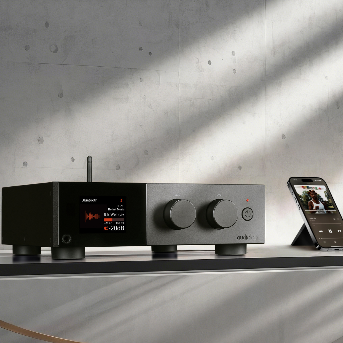 Een zwarte audio-ontvanger geeft muziekinformatie weer. Een telefoon speelt muziek af. Betonnen muurachtergrond.