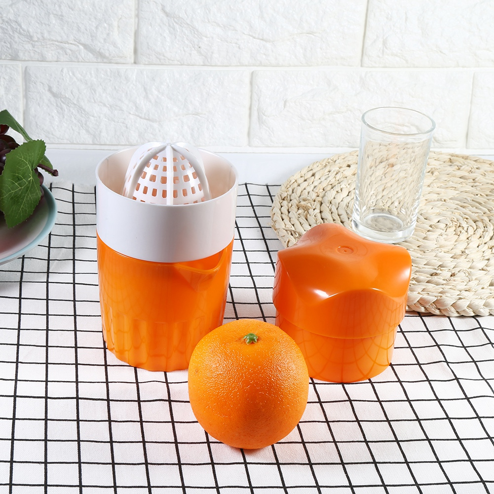 Eine Orange und ein Entsafter auf einem karierten Tuch. Der Entsafter ist orange und weiß, mit einem sternförmigen Deckel und einem Glas in der Nähe.