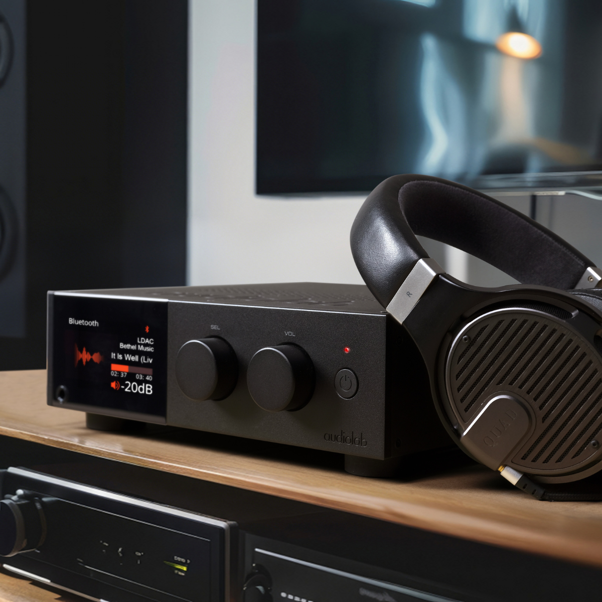 Een zwarte audioversterker met koptelefoon ligt op een houten oppervlak. De versterker toont muziekinformatie en heeft knoppen.