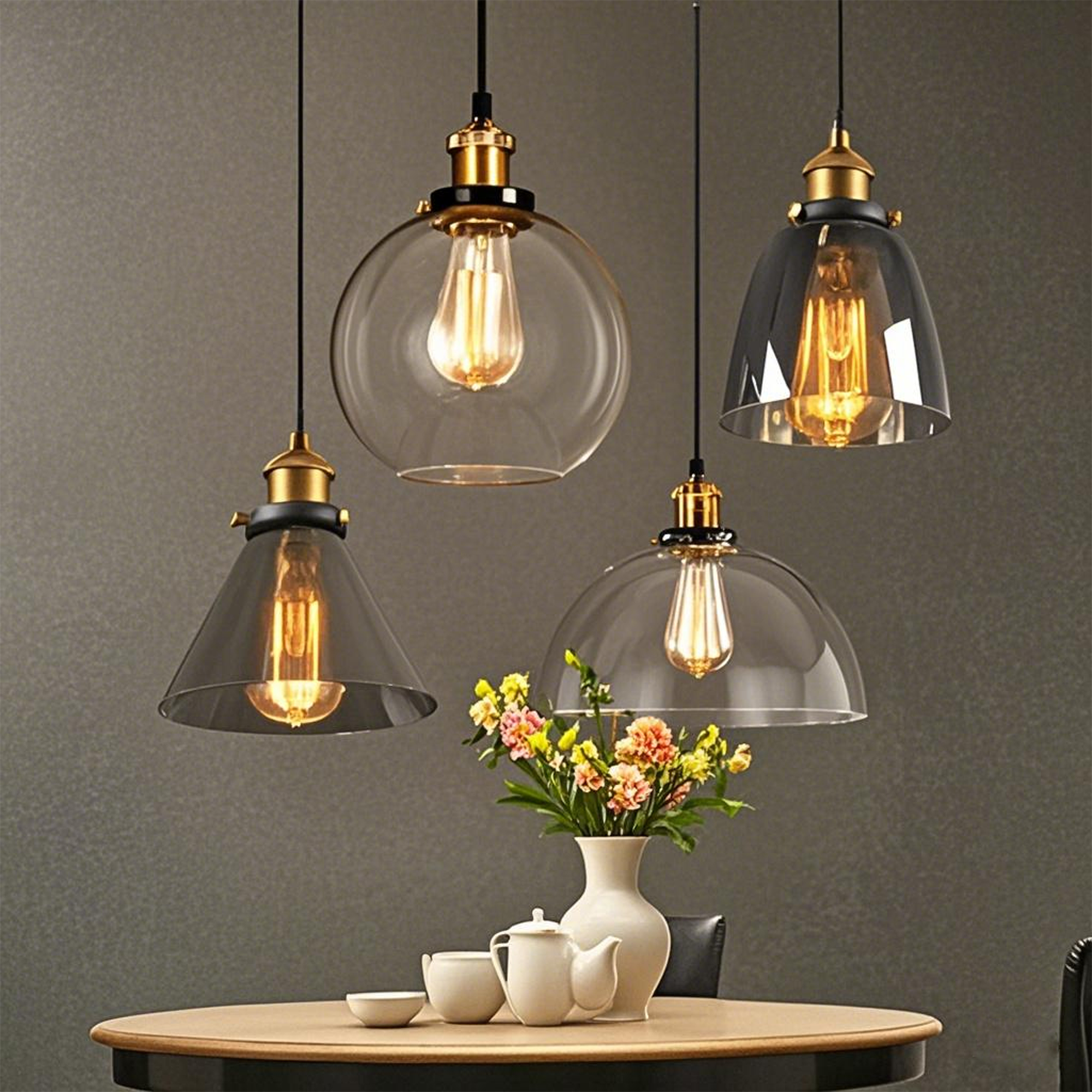 Vier Pendelleuchten mit Edison-Glühbirnen über einem Tisch mit einer Blumenvase und einem Teeservice. Die Leuchten haben unterschiedliche Formen.