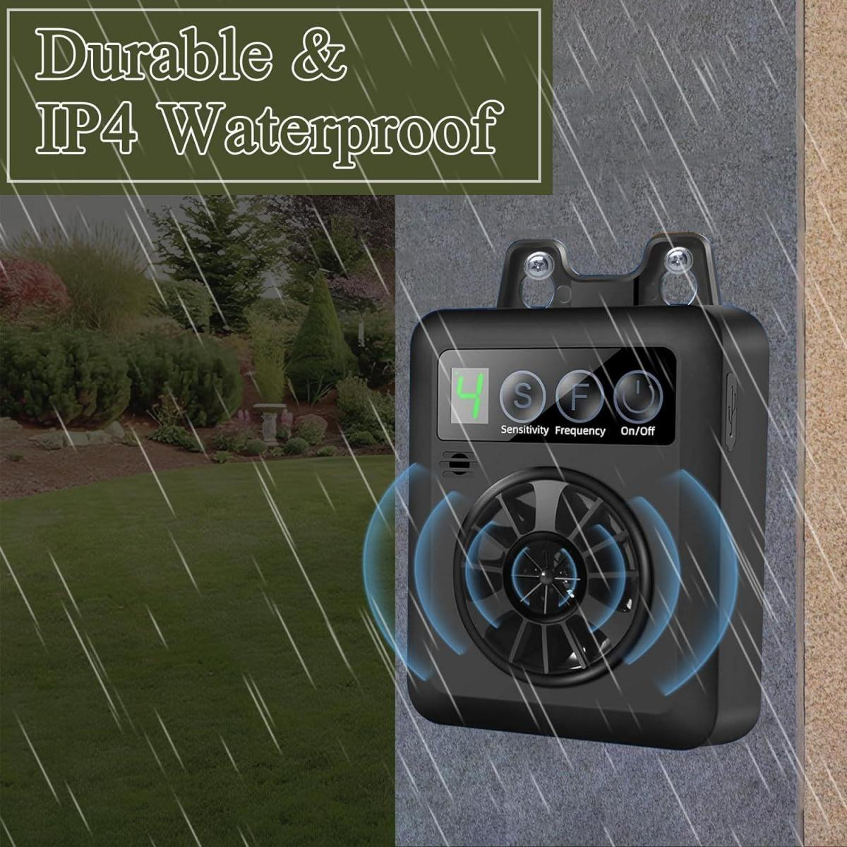 Schwarzes Gerät an der Wand, mit der Aufschrift Durable & IP4 Waterproof. Das Gerät hat Knöpfe, im Hintergrund ein Rasen mit Regen.