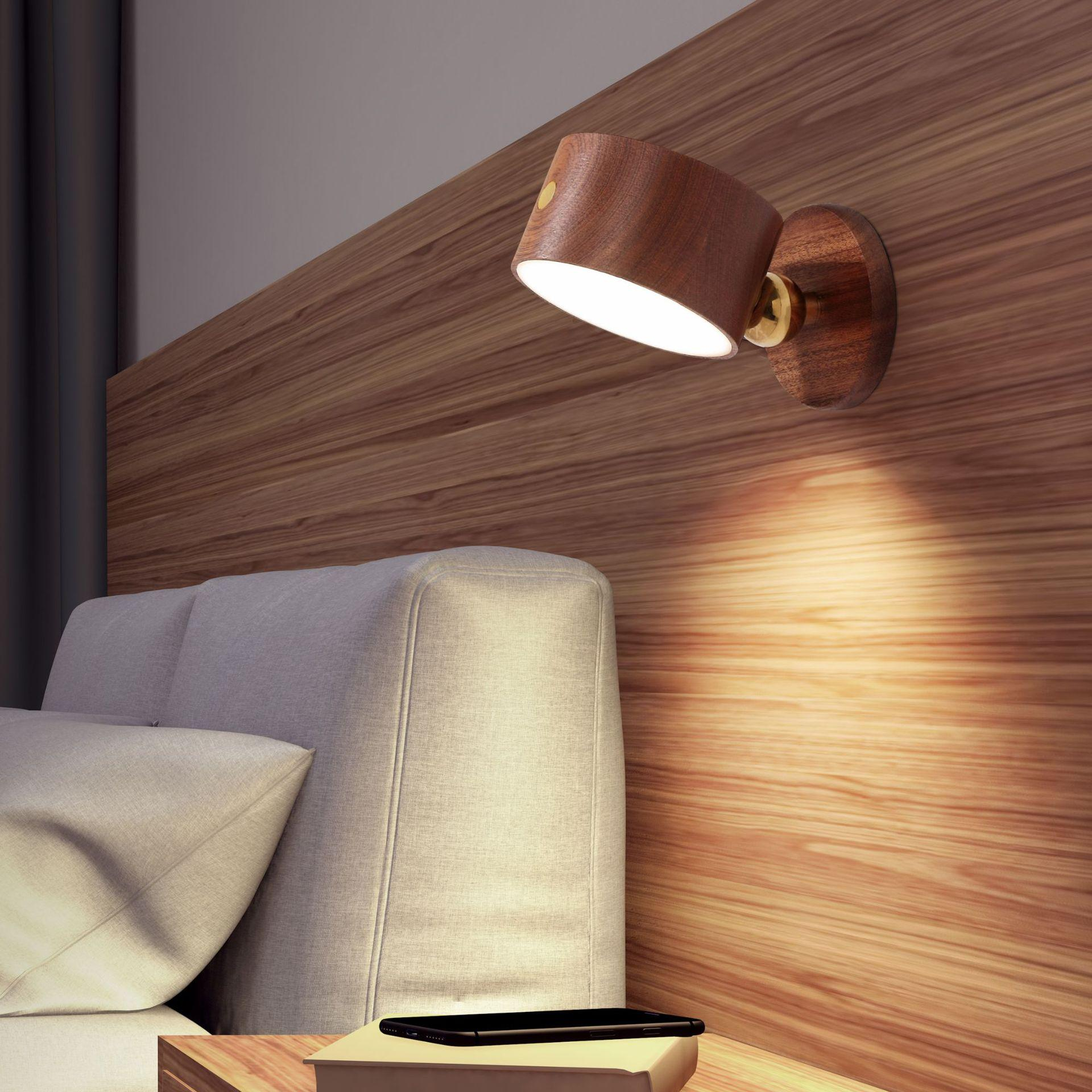 Eine Wandlampe aus Holz beleuchtet ein Bett in einem Raum. Ein Telefon liegt auf einem Nachttisch. Holzvertäfelung ist sichtbar.