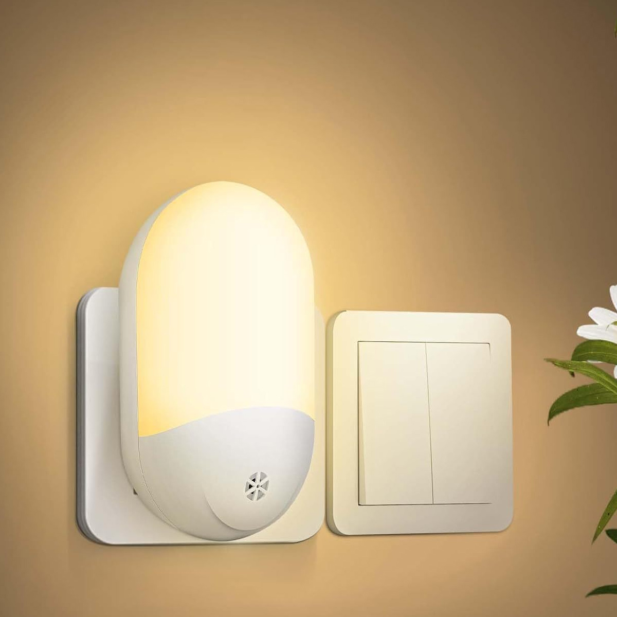 Ein weißes Nachtlicht, das in eine Wand gesteckt wird, neben einem Lichtschalter. Das Nachtlicht ist an und leuchtet. Die Wand ist beige.
