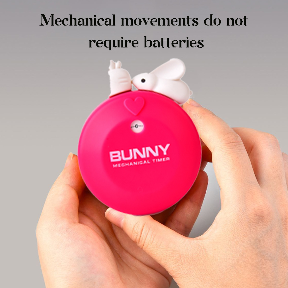 Ein pinkfarbener mechanischer Hasen-Timer wird gehalten. Er hat einen Hasen oben und einen Text, der lautet: „Mechanische Bewegungen benötigen keine Batterien.“