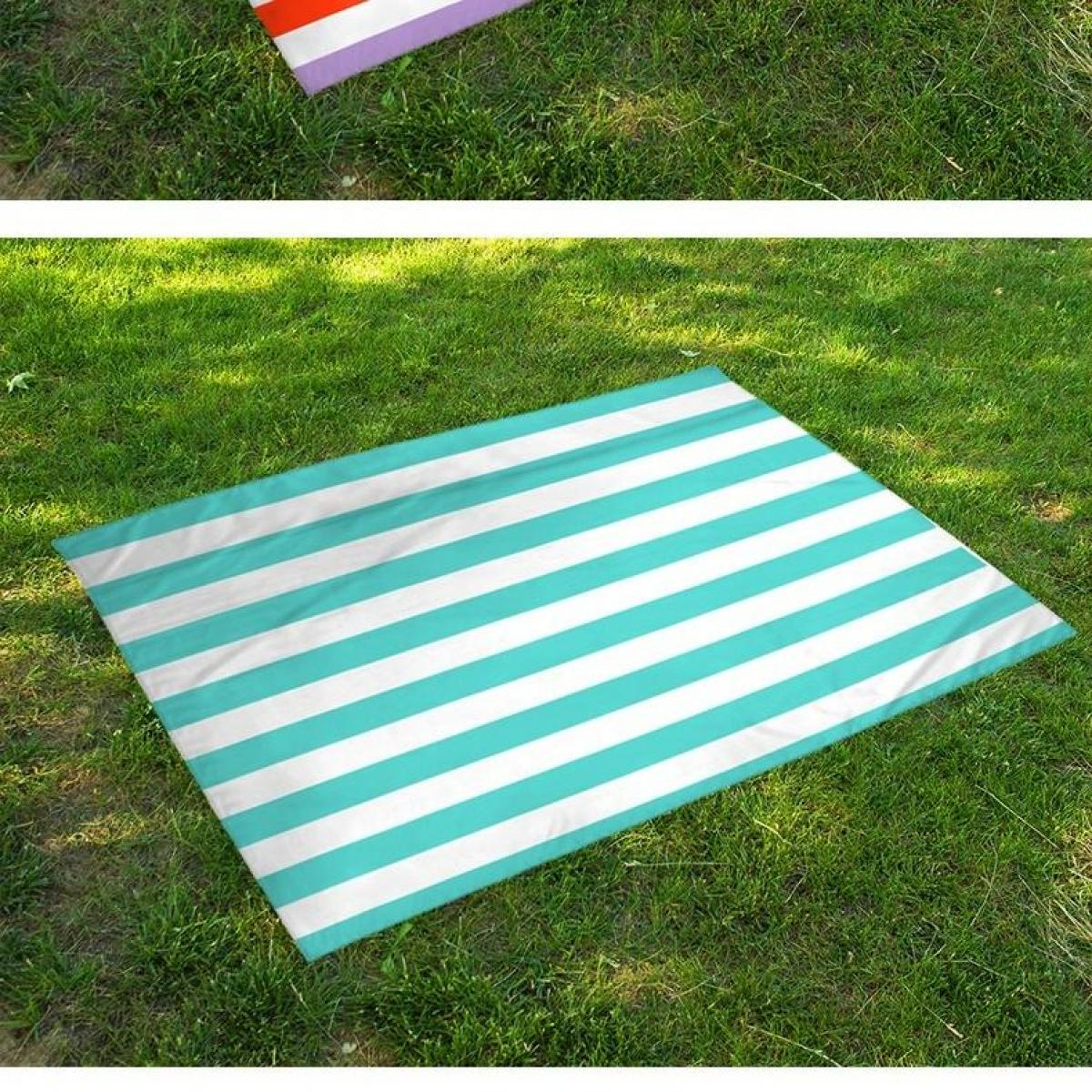 Eine Picknickdecke mit türkis-weißen Streifen liegt auf grünem Gras. Eine weitere kleinere Decke mit rot, weiß und lila Streifen liegt obenauf.