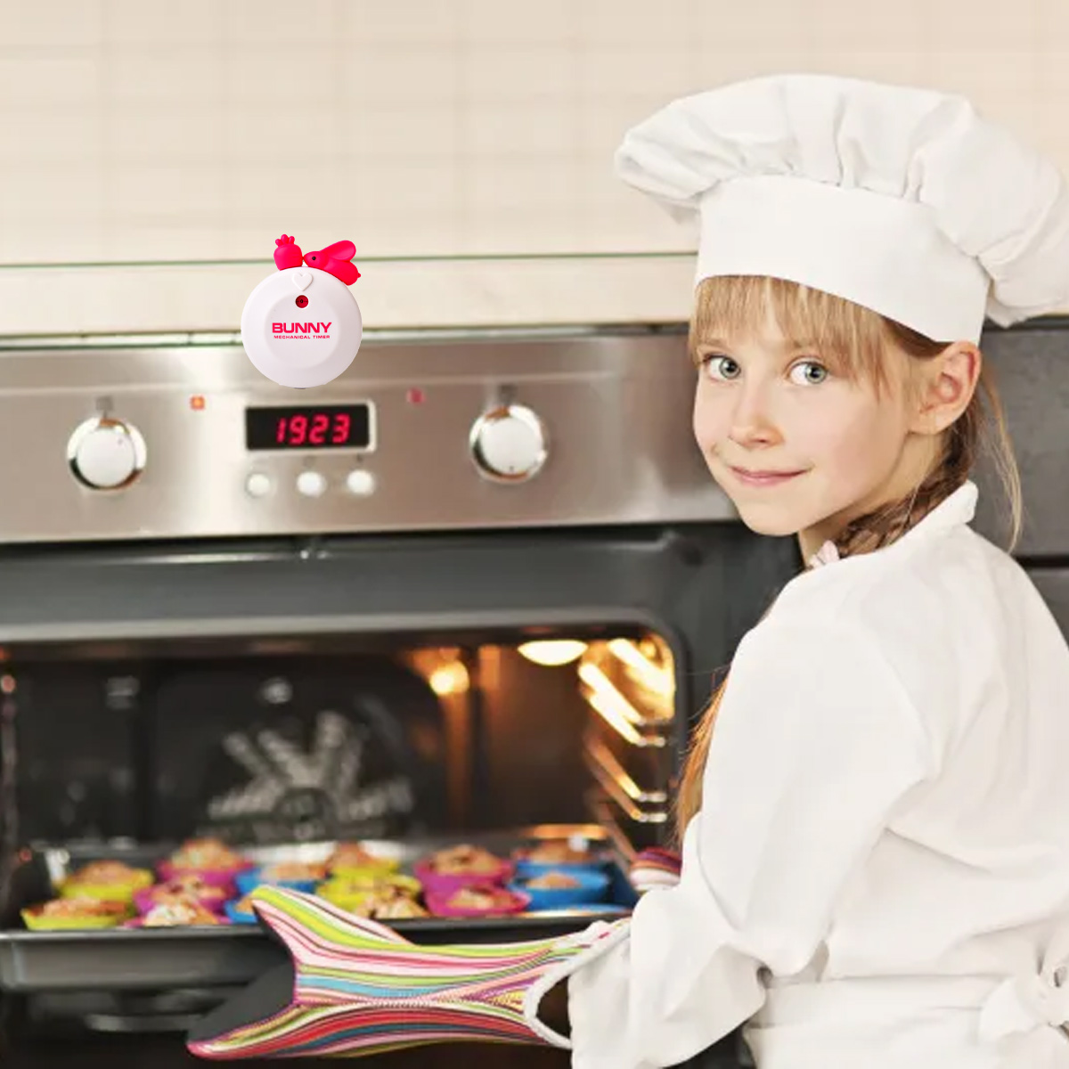 Ein junges Mädchen in Kochuniform lächelt und schaut in die Kamera. Sie hält ein Tablett mit Muffins aus dem Ofen.