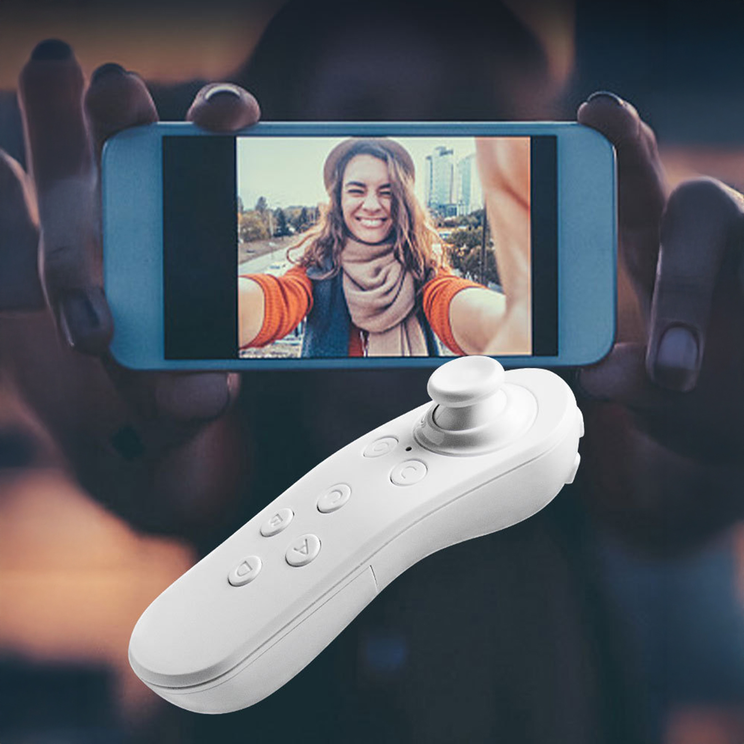 Persona che tiene in mano un telefono che mostra un selfie. Telecomando bianco in primo piano. Persona nel selfie sorridente con cappello e sciarpa.