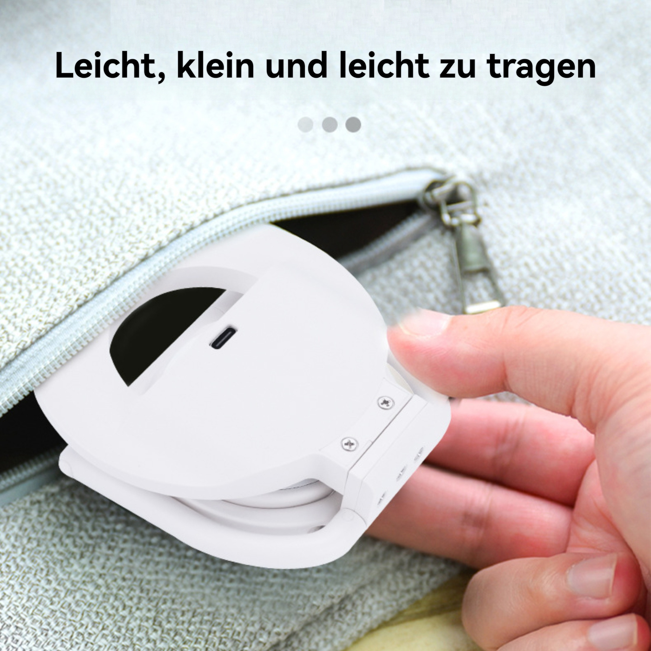 Eine weiße, faltbare Lampe wird von einer Hand in der Nähe eines offenen Reißverschlusses gehalten. Der Hintergrund ist ein hellgrauer Stoff.