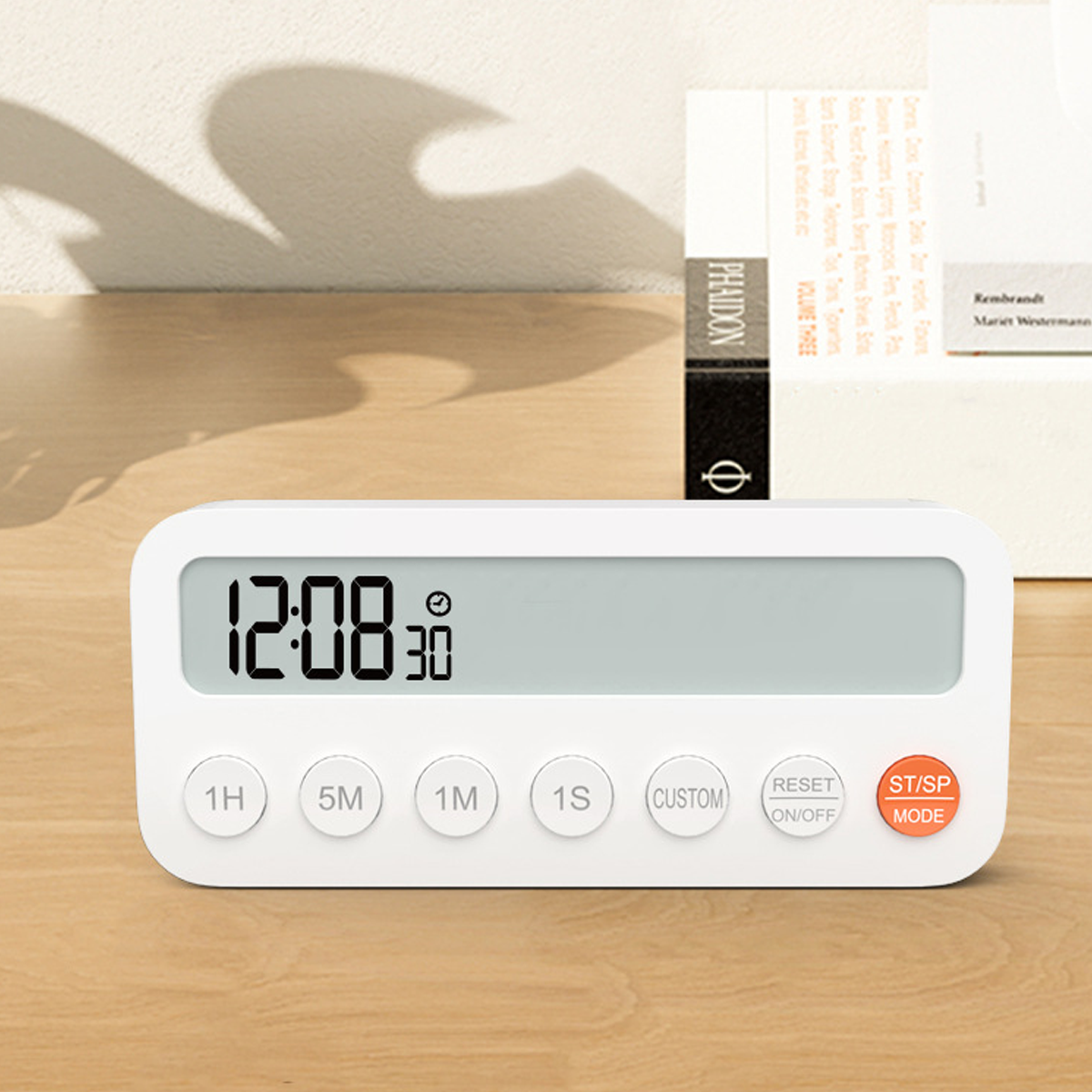 Weißer digitaler Küchentimer mit der Anzeige 12:08:30. Knöpfe: 1H, 5M, 1M, 1S, Custom, Reset und Start/Stopp. Bücher im Hintergrund.
