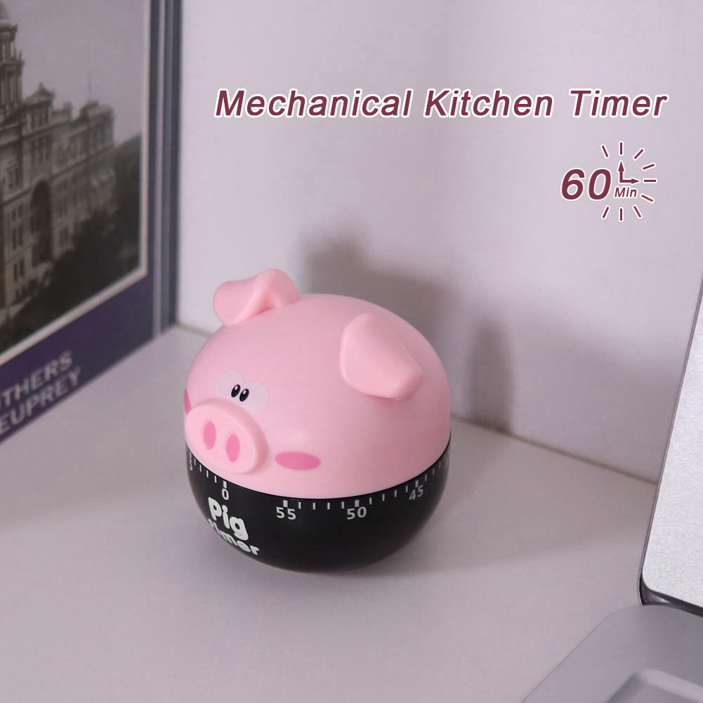 Ein rosa schweineförmiger Küchentimer steht auf einer weißen Oberfläche. Schwarze Basis mit Zahlen. Text: 'Pig Timer'. Dekotext: 'Mechanical Kitchen Timer'.