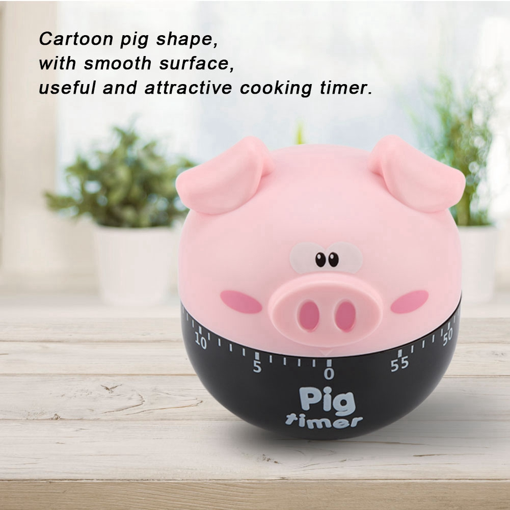 Ein rosa, schweineförmiger Küchentimer mit schwarzem Sockel. Er hat Augen, Ohren und eine Nase. Er steht auf einer hellen Holzoberfläche.