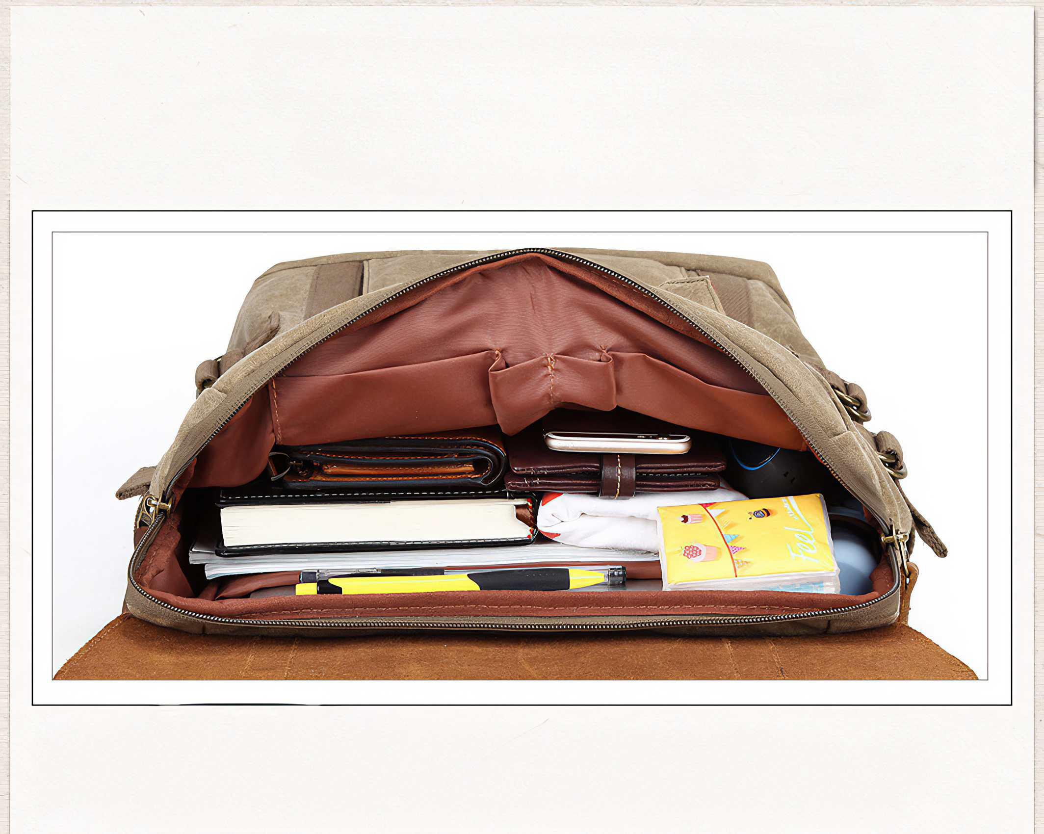 Offene, braune Canvas-Tasche gefüllt mit Gegenständen: Geldbörsen, Telefon, Notizbücher, Stift und ein kleines gelbes Notizbuch. Weißer Hintergrund.