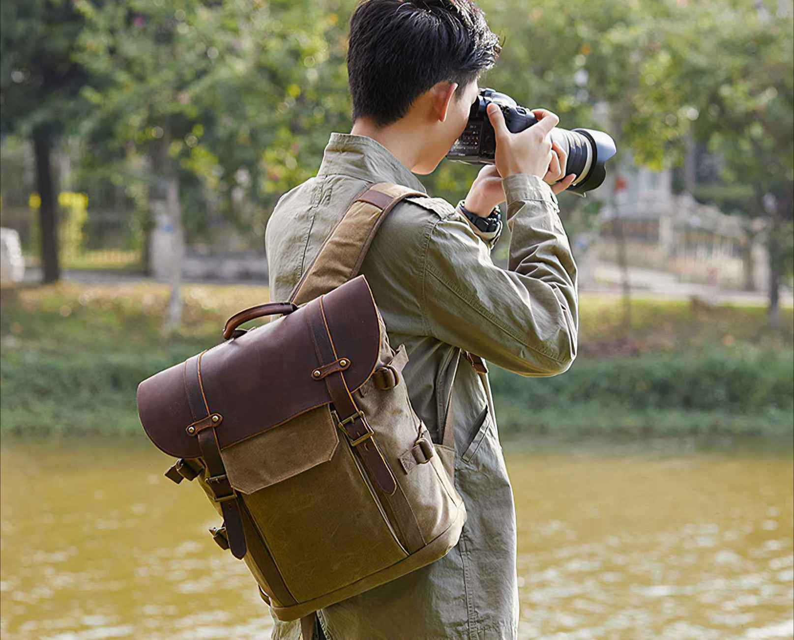 Ein Mann fotografiert. Er hat einen Rucksack und trägt eine Jacke. Ein Gewässer und Bäume sind im Hintergrund.