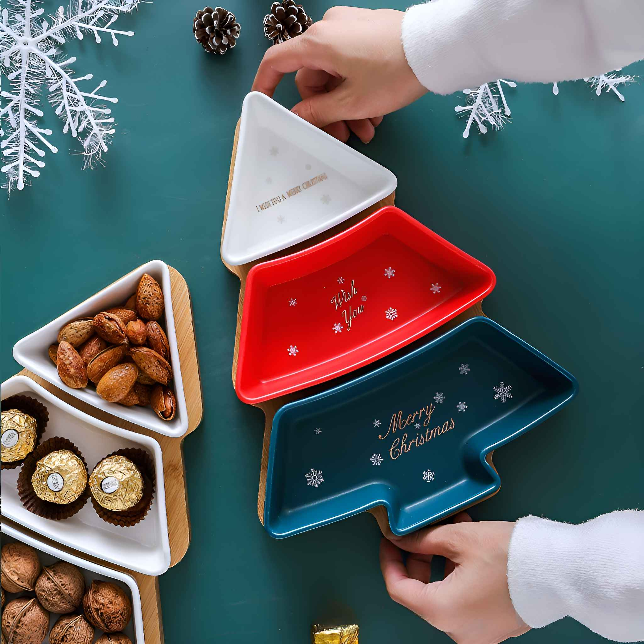 Weihnachtsbaumförmige Servierschalen. Weiße, rote und blaue Schalen mit Text und Essen. Hände halten den Baum.
