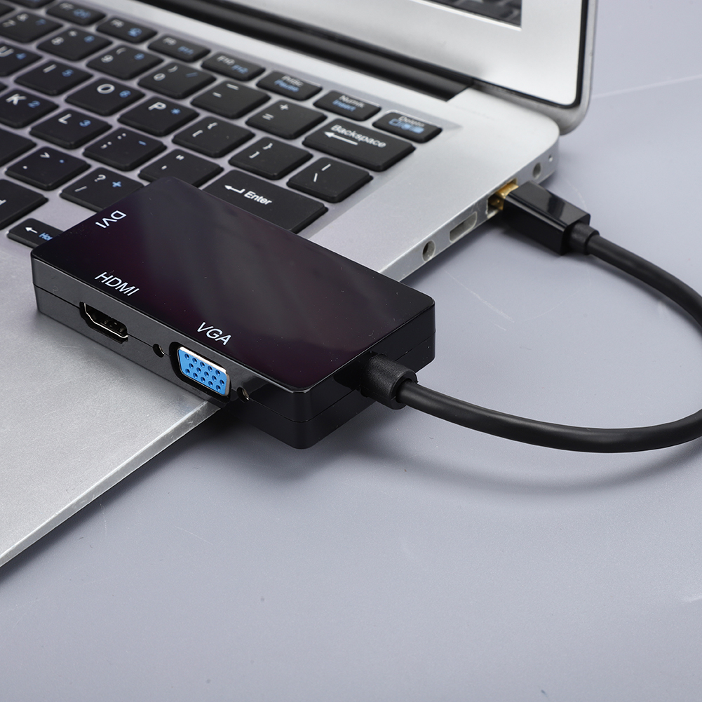 Ein schwarzer Adapter mit HDMI-, VGA- und DVI-Anschlüssen, der über ein schwarzes Kabel mit einem Laptop verbunden ist. Die Tastatur des Laptops ist sichtbar.
