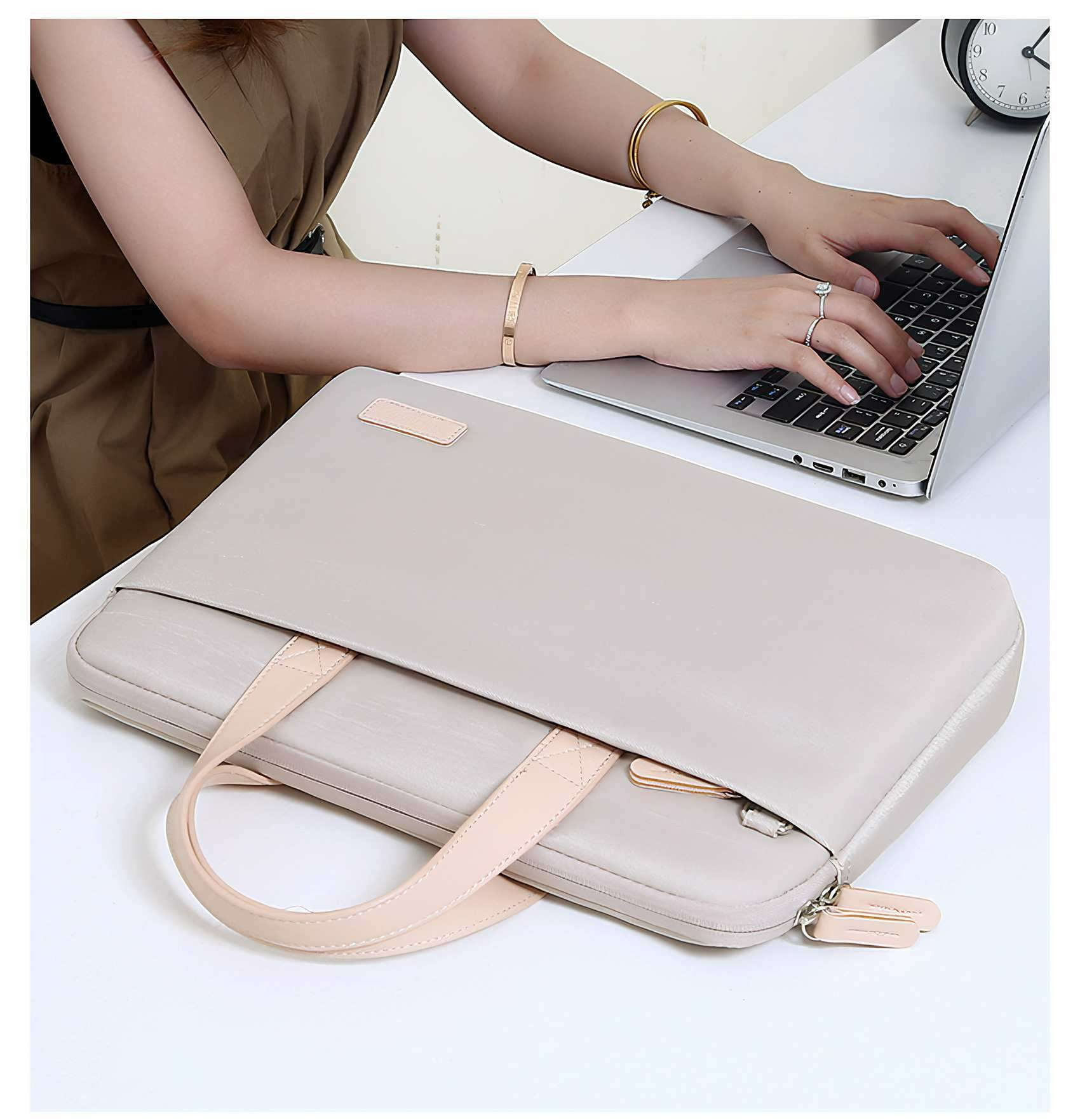 Eine Person tippt auf einem Laptop. Eine beige Laptoptasche und eine Uhr sind ebenfalls auf dem weißen Tisch zu sehen.