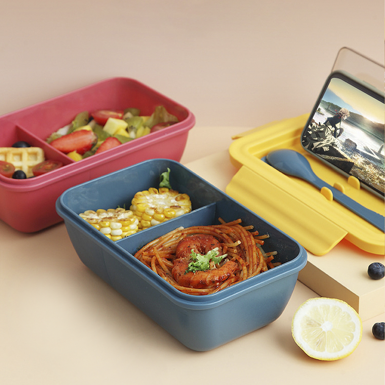 Cajas de almuerzo con comida: ensalada, gofre, fruta, maíz, pasta, camarones y un limón. Teléfono mostrando un video.