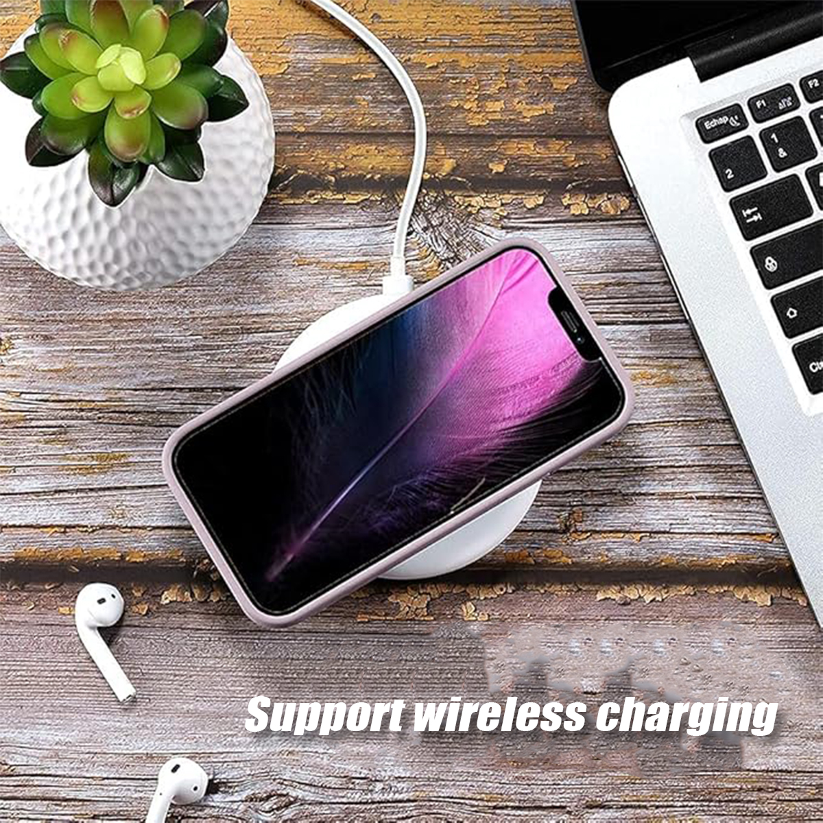 Telefon auf Ladegerät. Weiße Ohrhörer, Laptop und Pflanze auf Holzoberfläche. Text: Wireless Charging unterstützen.