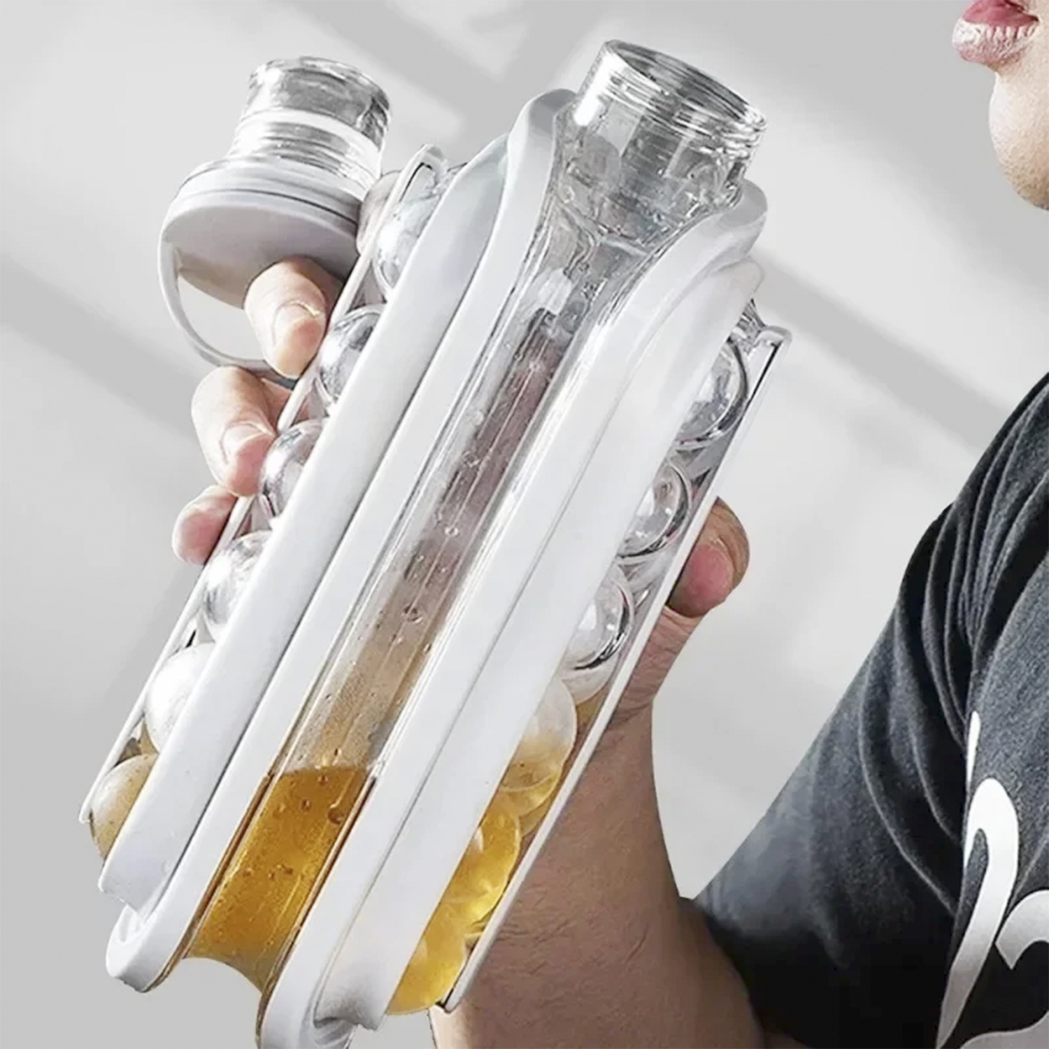 Persona che tiene un contenitore di plastica bianco e trasparente con liquido giallo e palline di ghiaccio. Lo sfondo è bianco.