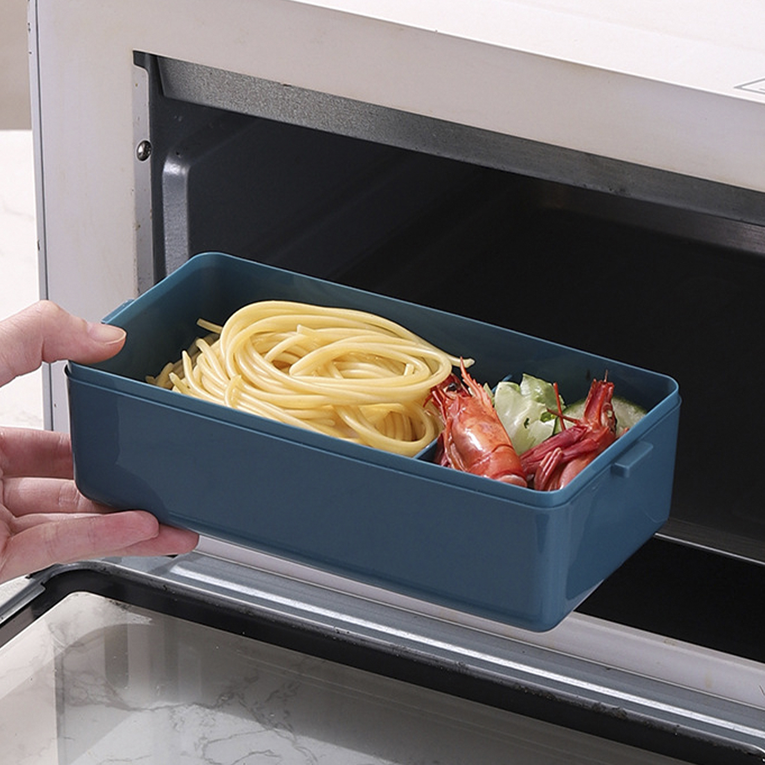 Una mano sostiene un recipiente azul con espaguetis y camarones, colocado dentro de un horno microondas.