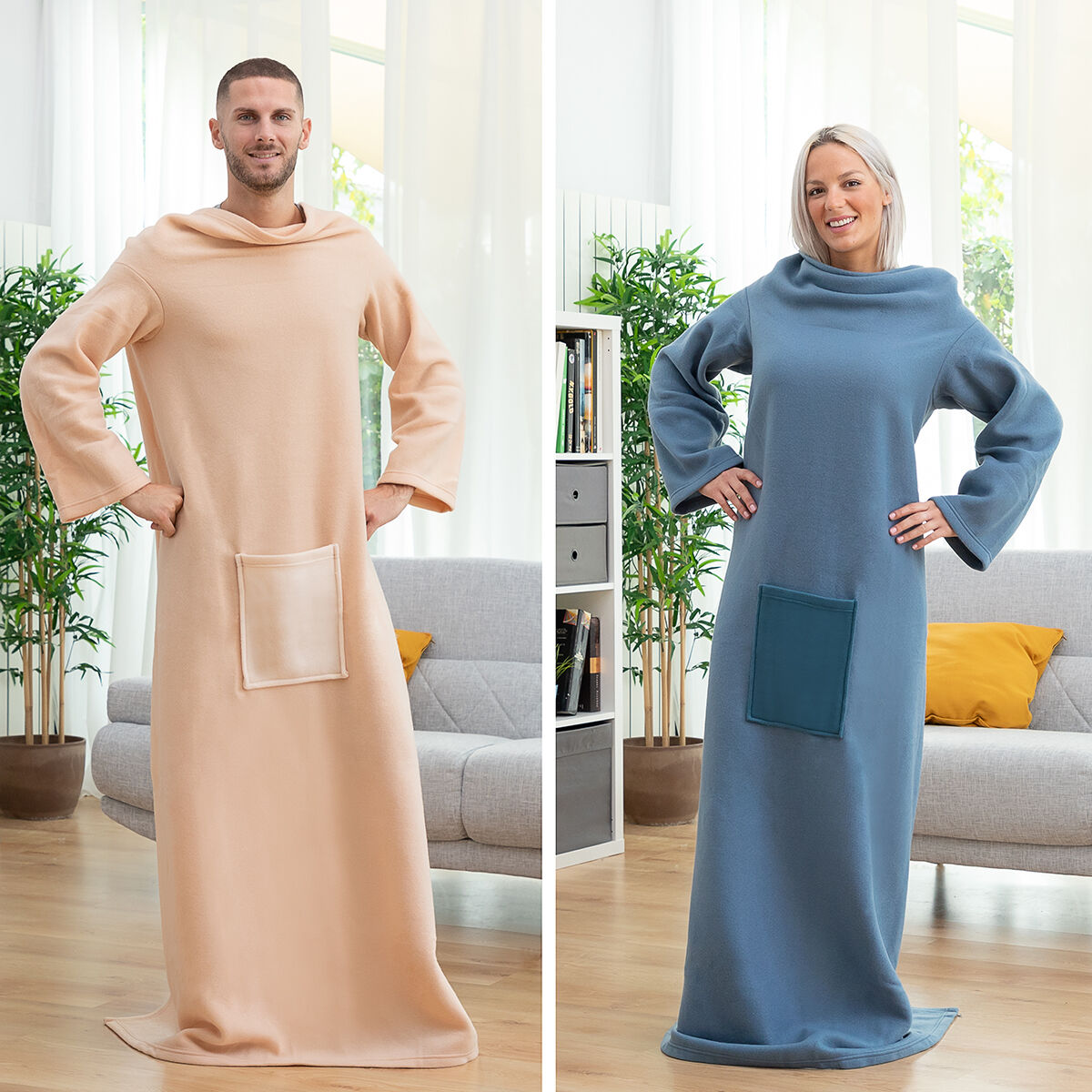 Zwei Personen in kuscheligen Decken stehen. Einer trägt Beige, der andere Blau. Beide haben Taschen. Hintergrund: Sofa, Pflanzen, Fenster.