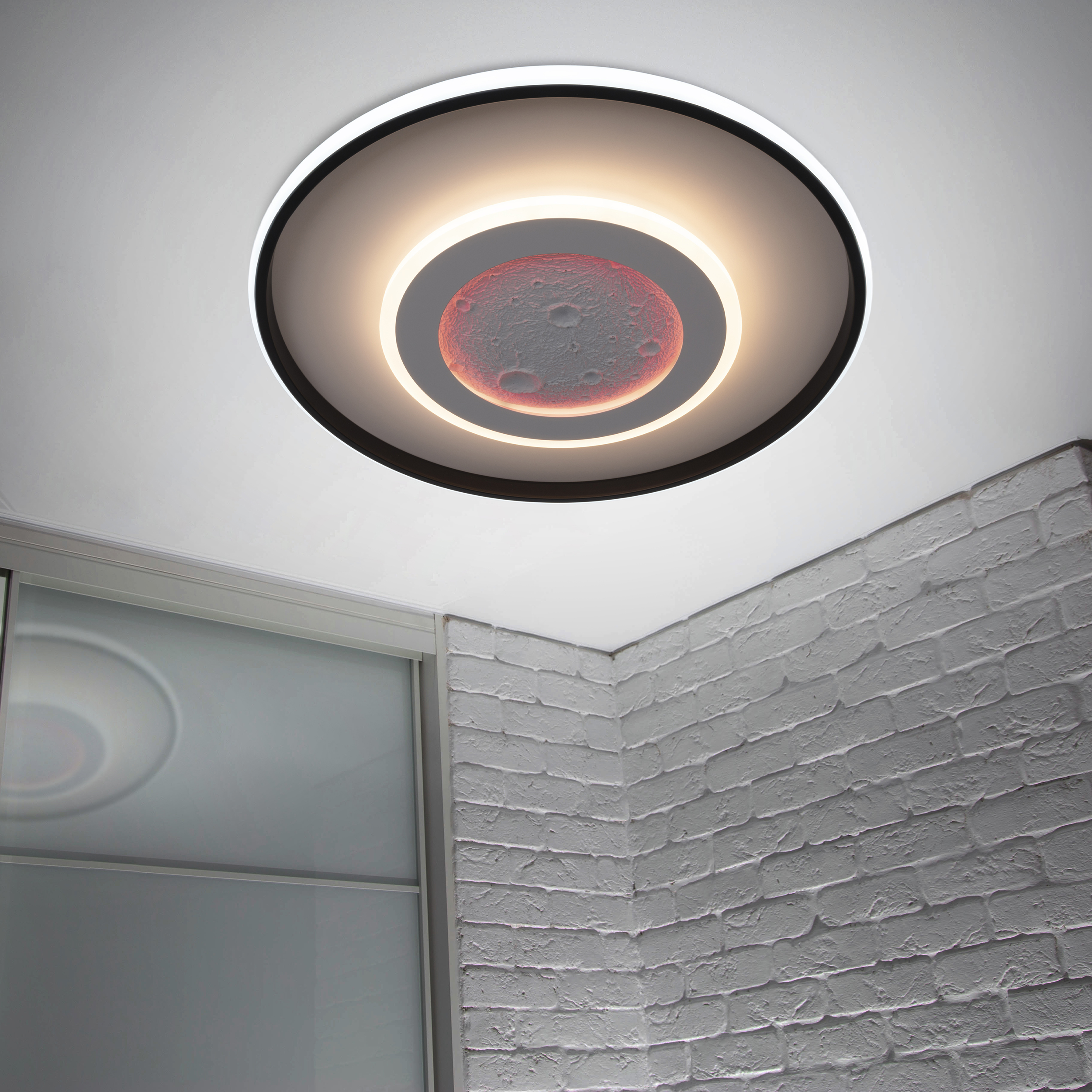 Deckenleuchte mit Monddesign. Weiße Decke, graue Ziegelmauer und ein Fenster. Das Licht ist kreisförmig.