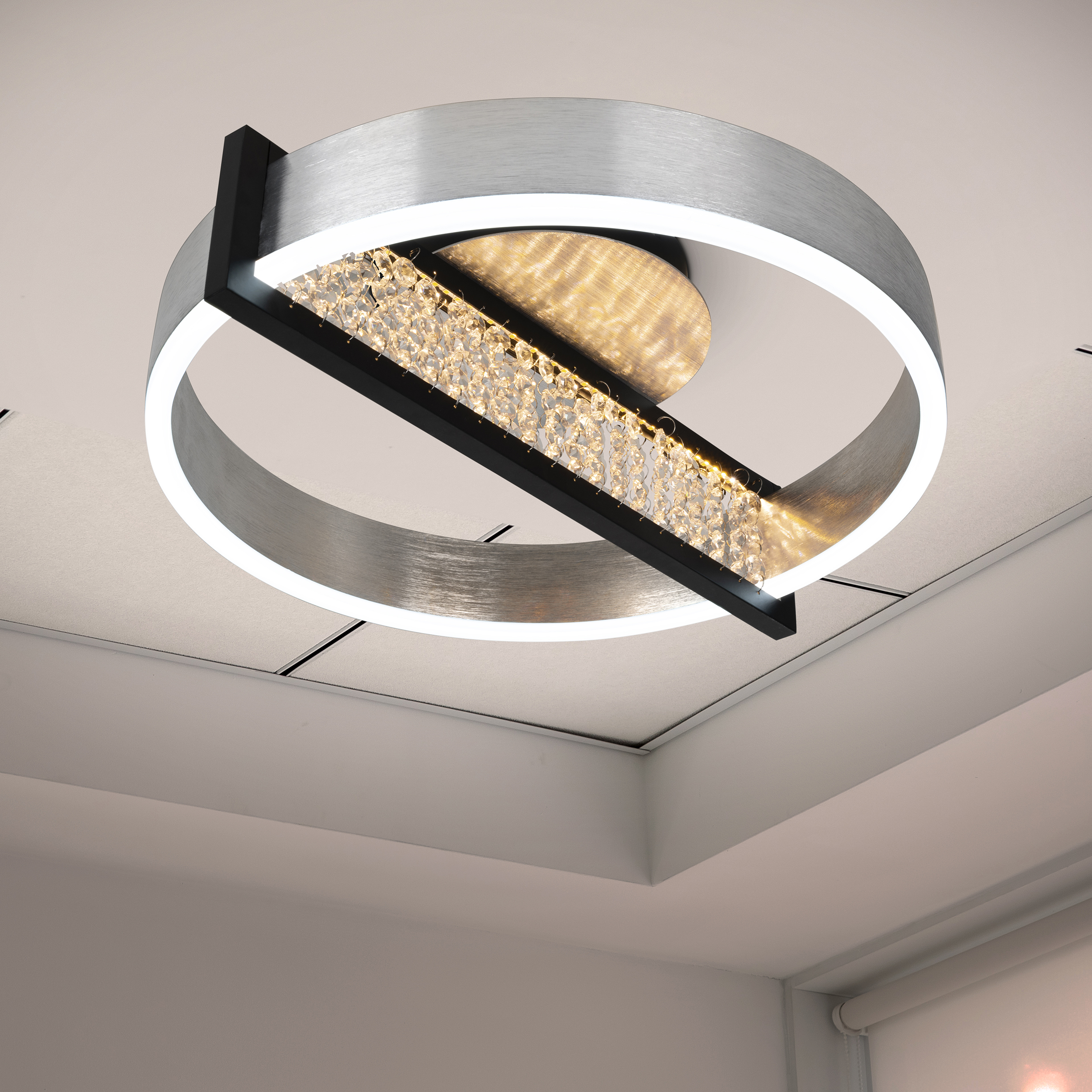 Moderne Deckenleuchte mit silbernem Ring und Kristallelementen. Hängt an einer weißen Decke.