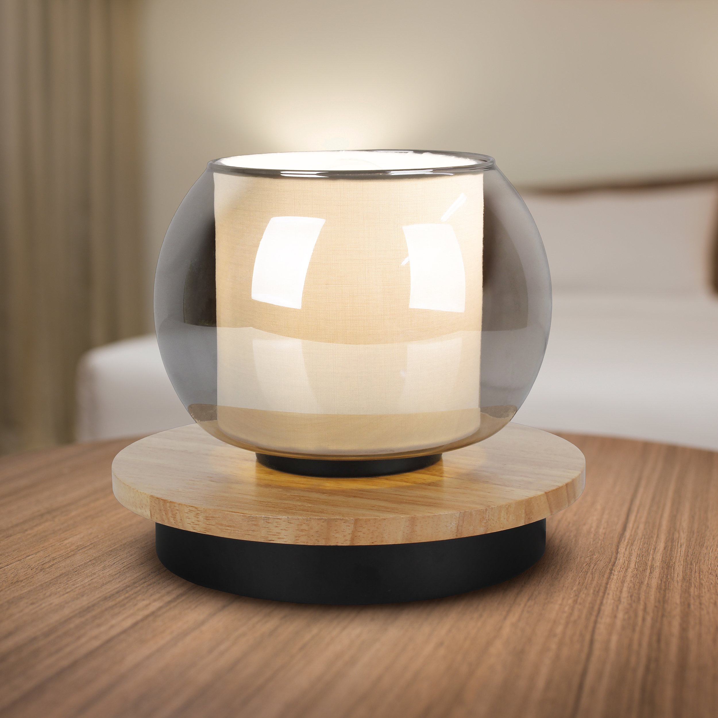Eine moderne Lampe mit Glasschirm, beigem Stoff und Holzsockel steht auf einem braunen Holztisch.