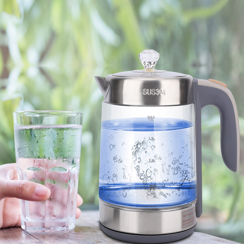Ein Glaskessel mit Wasser und ein Glas Wasser vor einem verschwommenen grünen Hintergrund. Eine Hand hält das Glas.