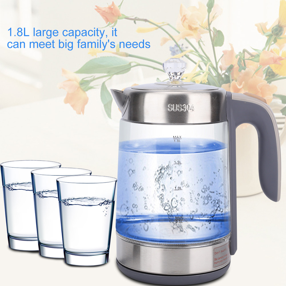 Ein Glaskessel mit Wasser, drei Wassergläser und Blumen im Hintergrund. Der Kessel ist aus Edelstahl und hat einen Griff.