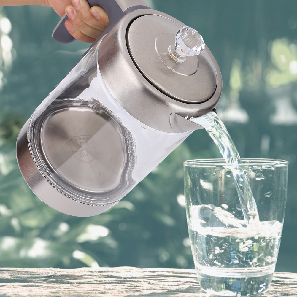 Eine Hand gießt Wasser aus einem Glaskessel in ein Glas. Der Hintergrund zeigt Grün durch ein Fenster.