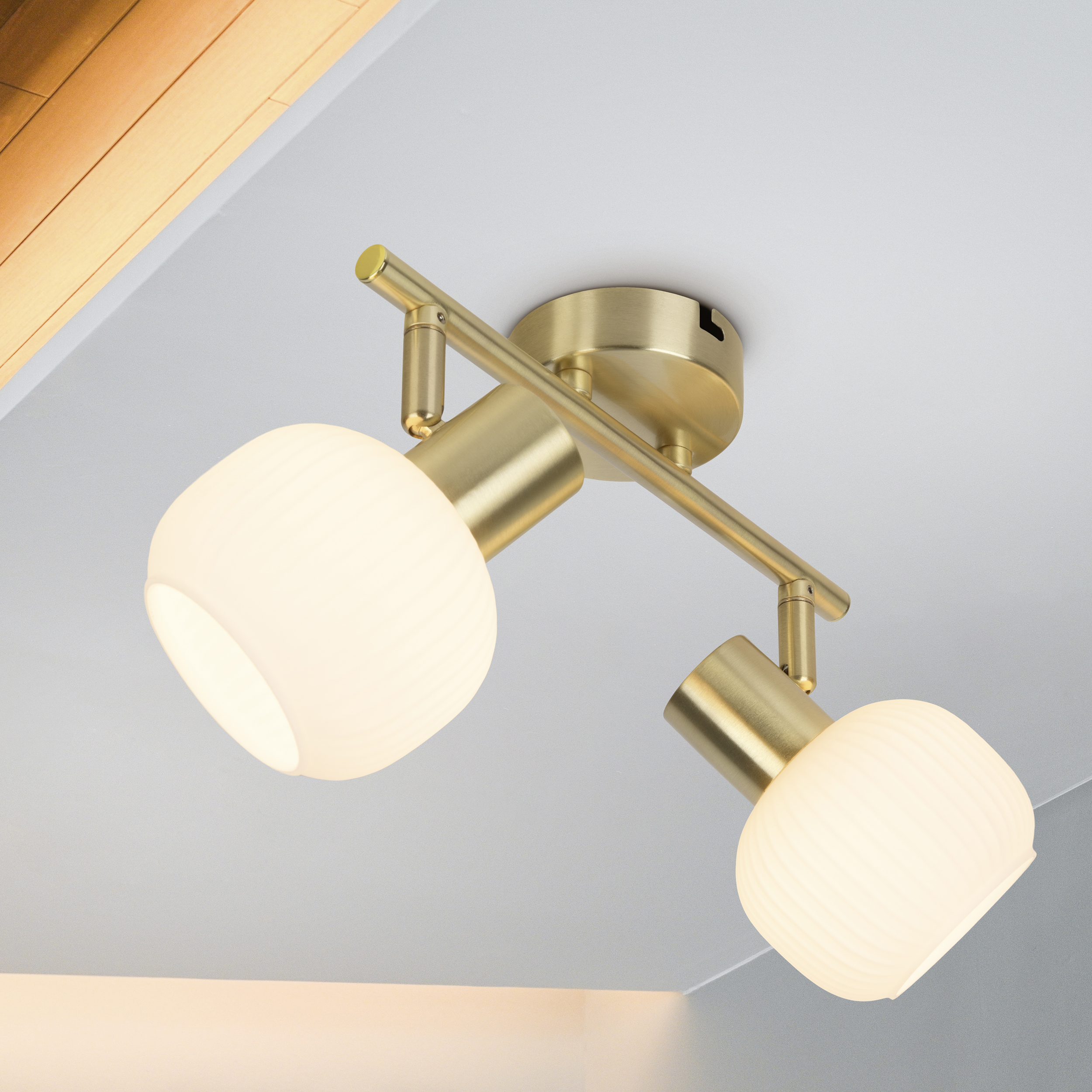Goldfarbene Deckenleuchte mit zwei weißen, abgerundeten Lampen. Der Hintergrund ist eine weiße Decke und Holzpaneel.