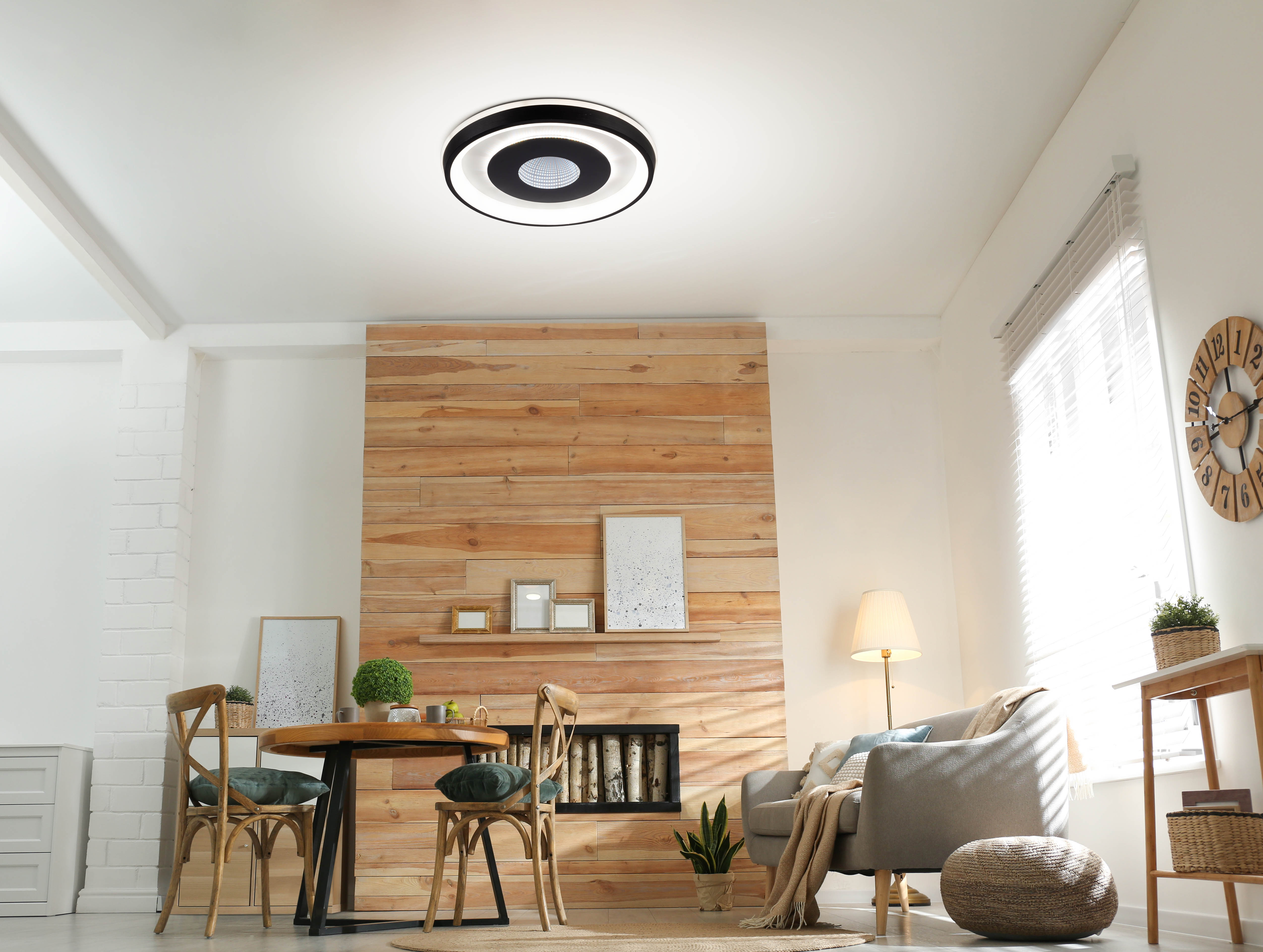 Wohnzimmer mit Holzwand, rundem Tisch, Stühlen, Sofa und großer Deckenleuchte.
