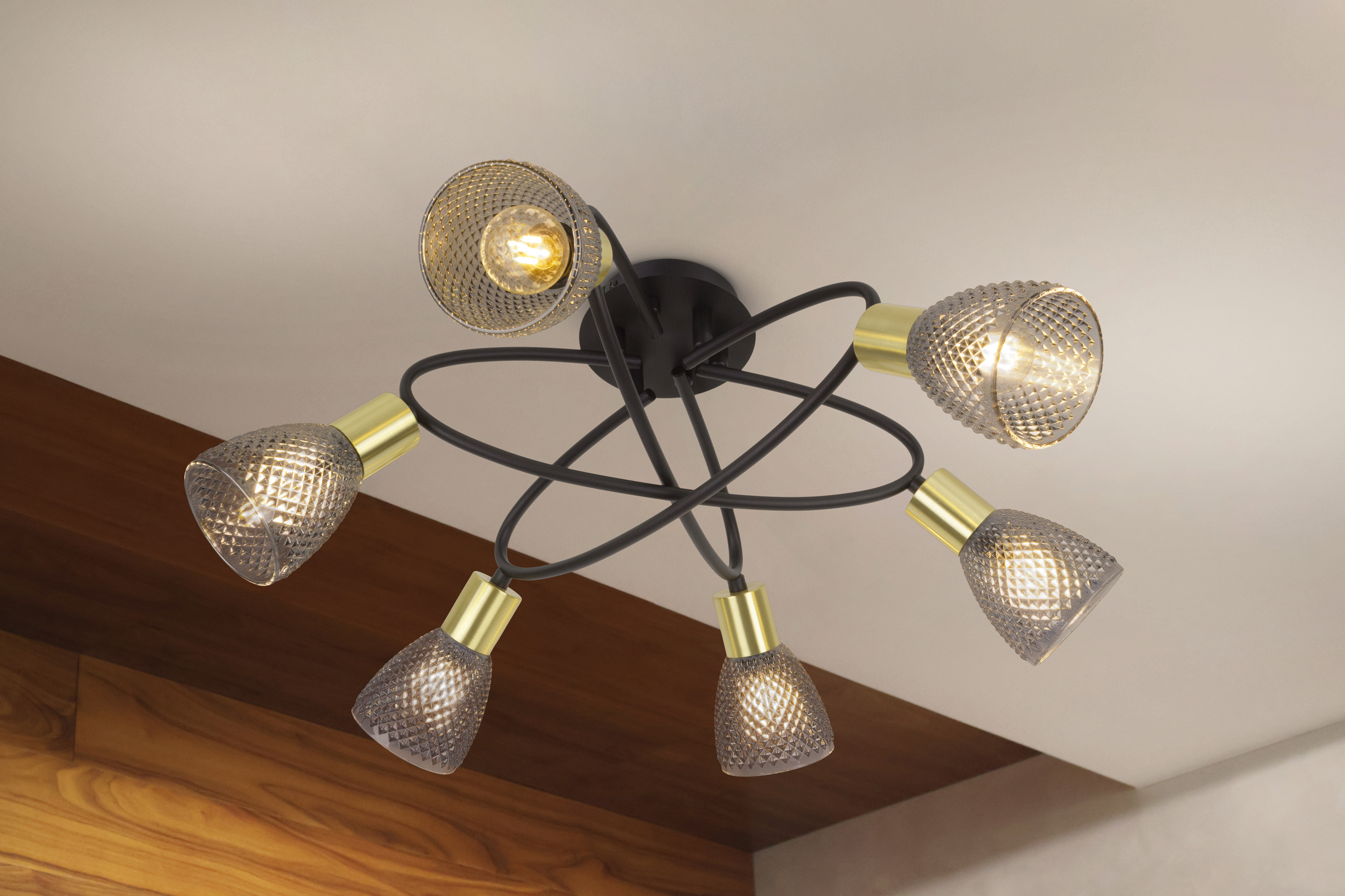 Eine Deckenleuchte mit sechs Lampen. Sie hat einen schwarzen Rahmen, goldfarbene Lampenhalterungen und gemusterte Glasschirme. Der Hintergrund ist weiß.