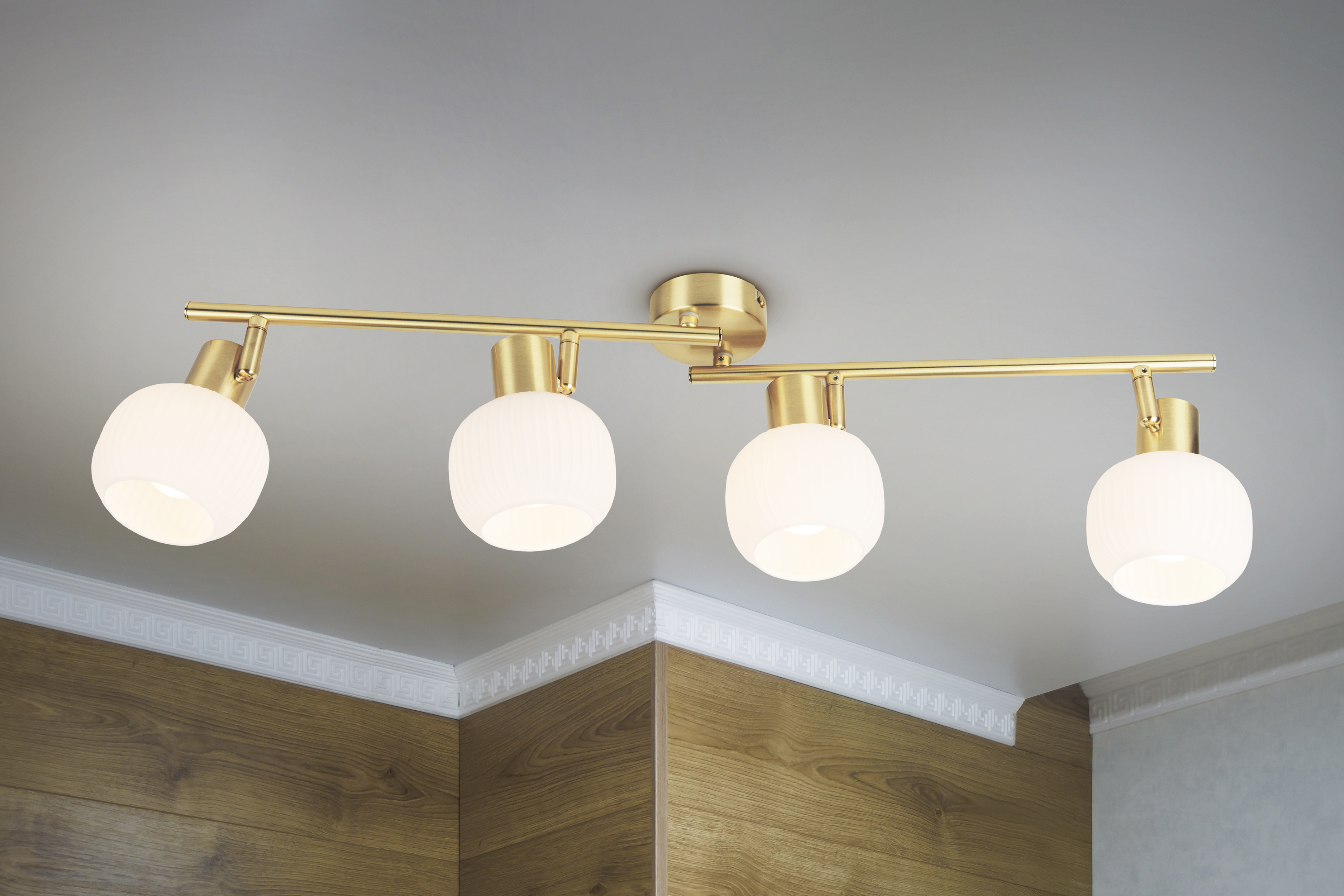 Eine Deckenleuchte mit vier runden, weißen Lampen. Sie ist goldfarben und an einer weißen Decke installiert.