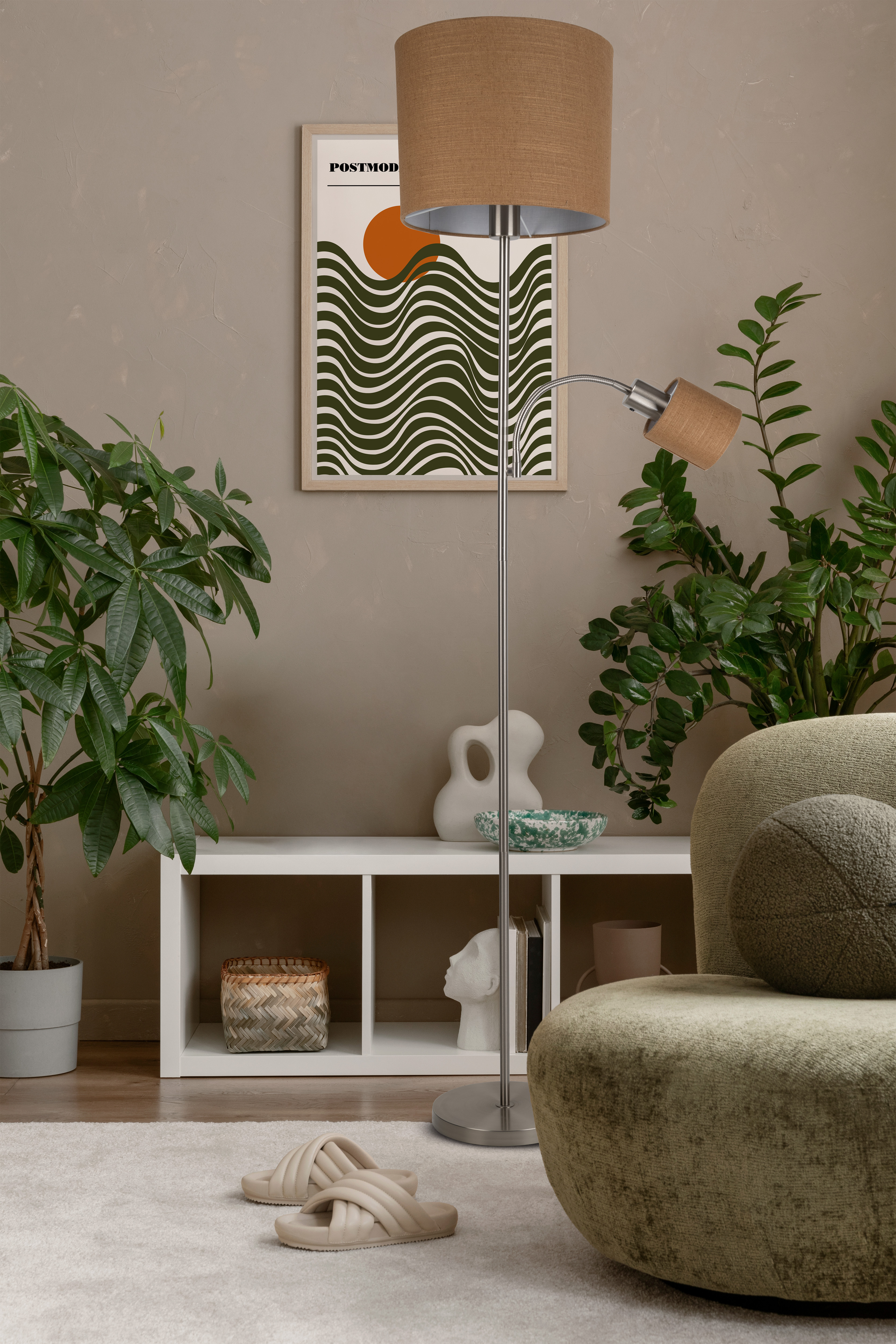 Ein Raum mit Pflanzen, einer Couch, einer Lampe und einem Poster. Hausschuhe auf dem Boden.