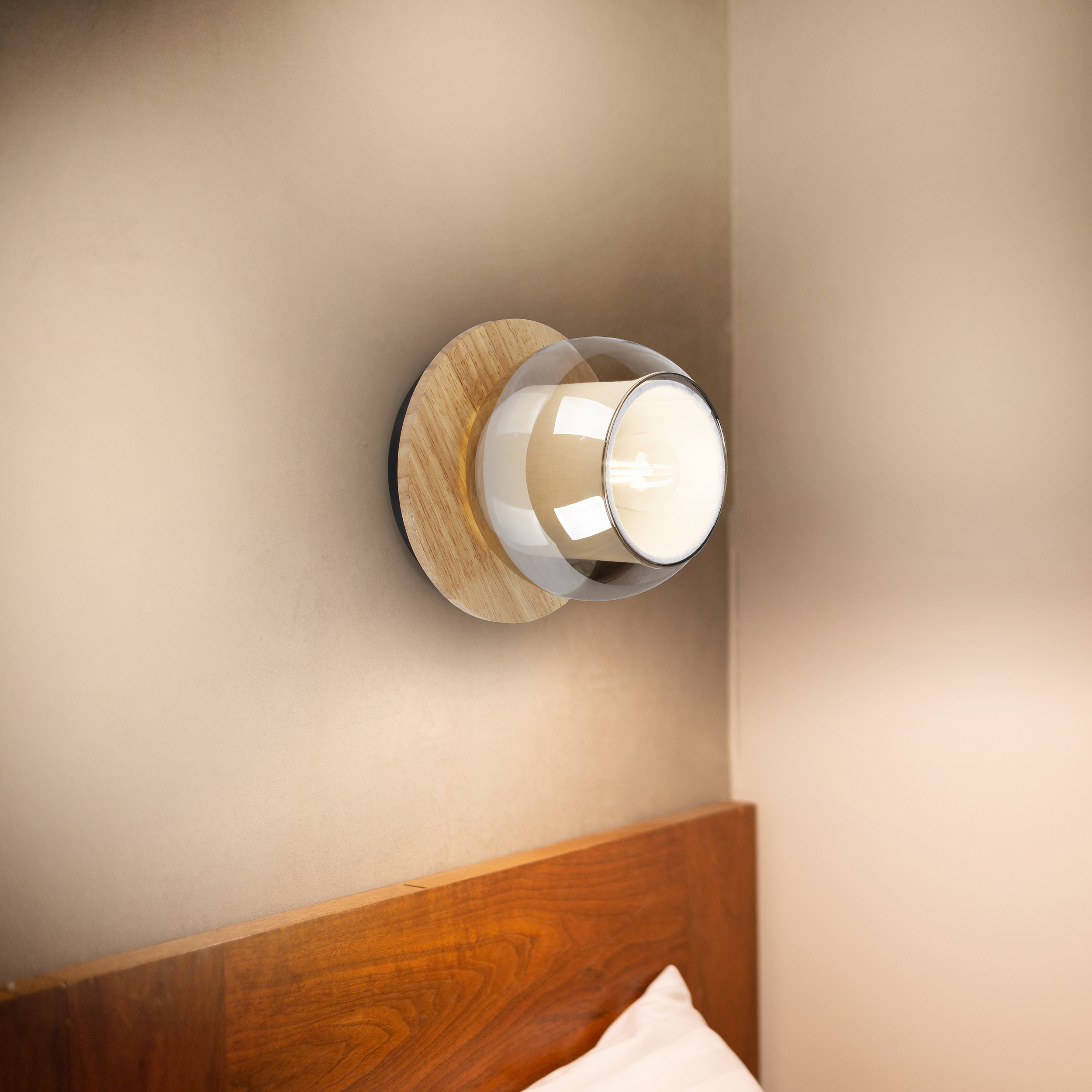 Eine Wandlampe mit Holzsockel und Glasschirm befindet sich über einem hölzernen Kopfteil mit einem weißen Kissen.