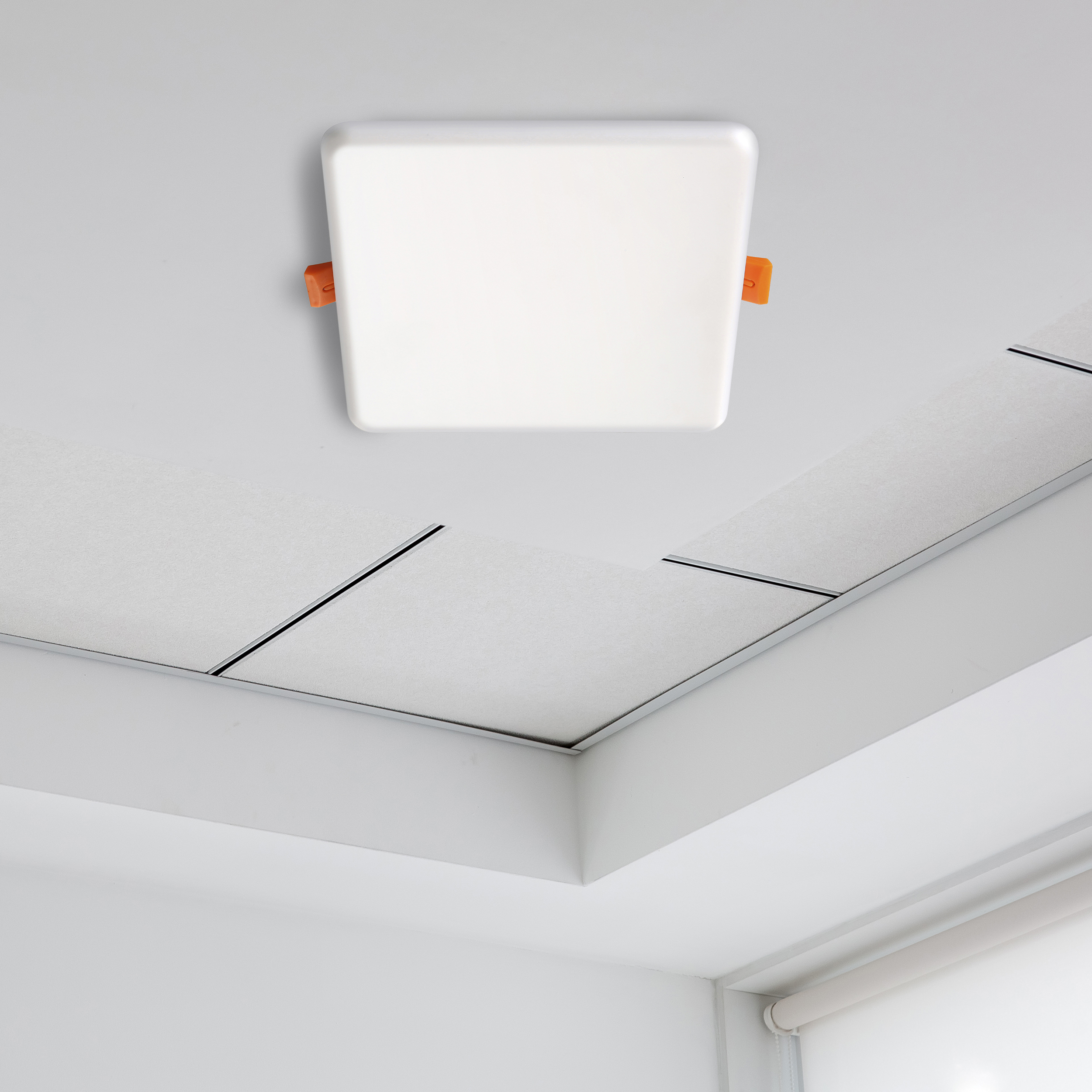 Eine quadratische, weiße Deckenleuchte mit orangefarbenen Clips ist an einer weißen Decke mit weißen Paneelen montiert.