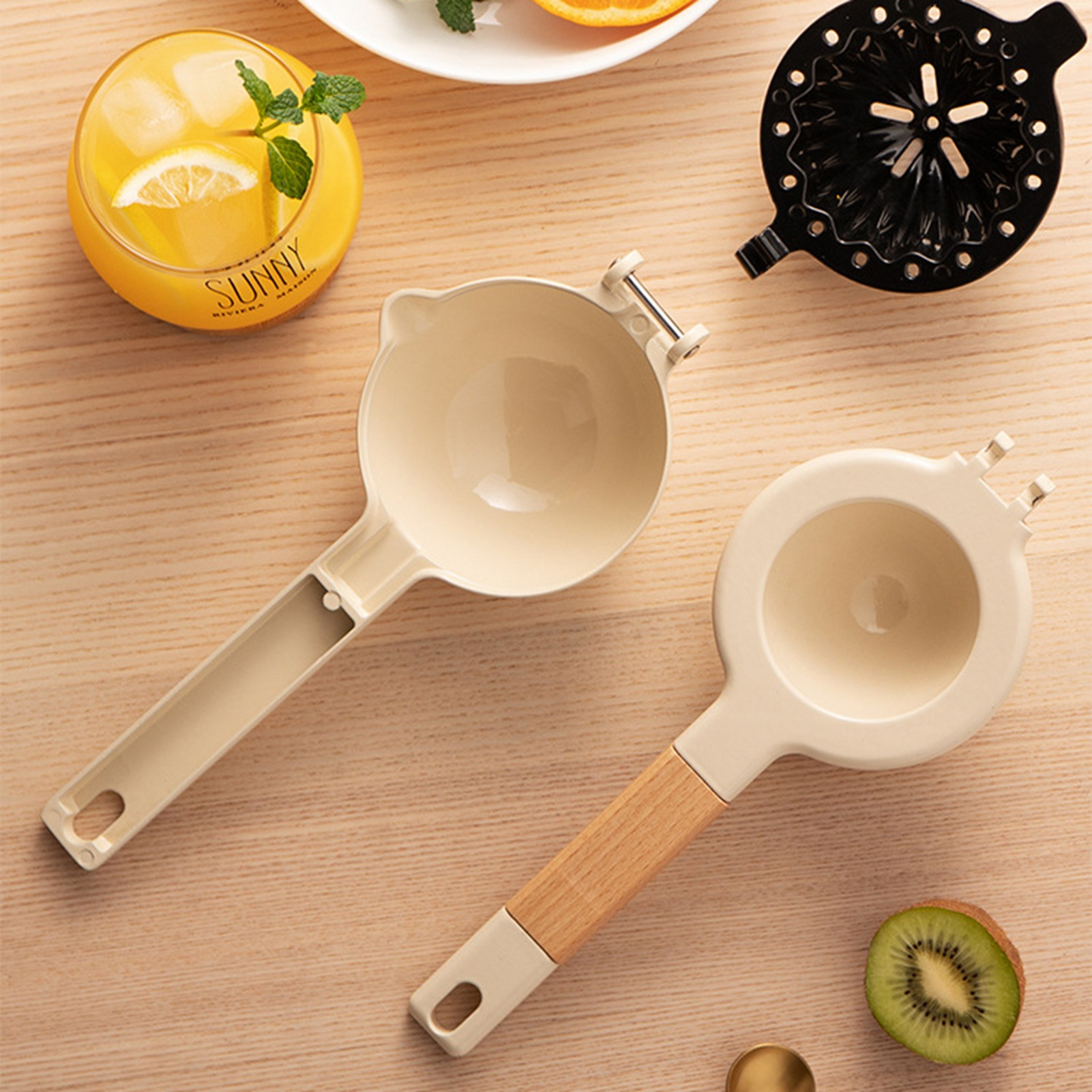 Das Bild zeigt ein Glas Saft mit Zitrone, zwei Entsafter, eine halbe Kiwi und andere Gegenstände auf einer Holzoberfläche.