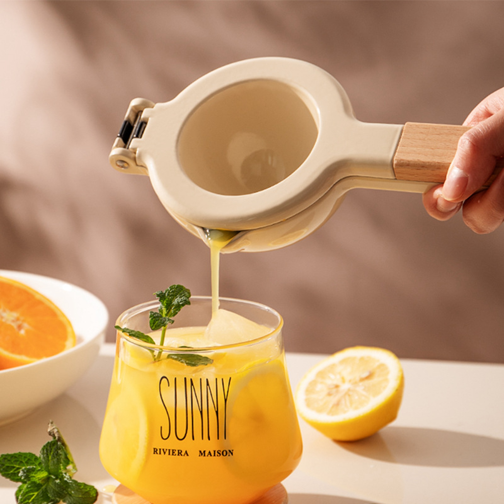 Eine Hand presst Zitronensaft in ein Glas gelbes Getränk. Eine Orangenscheibe und eine Zitronenhälfte sind sichtbar.
