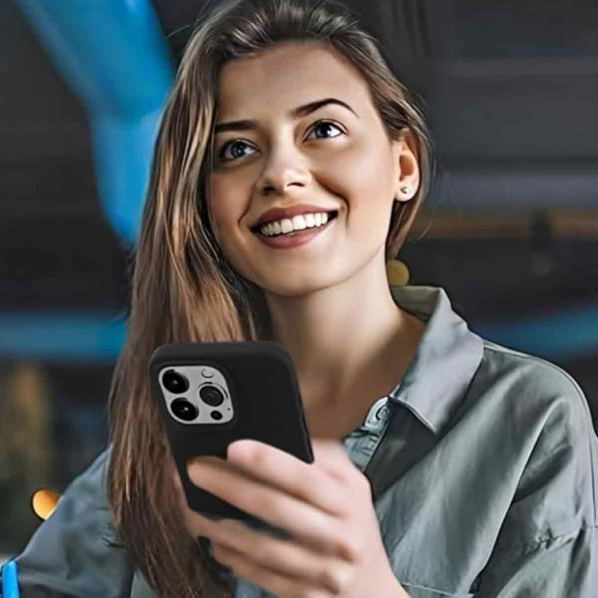 Lächelnde Frau hält ein schwarzes Telefon. Sie trägt ein graues Hemd. Der Hintergrund ist verschwommen, mit blauen und dunklen Tönen.